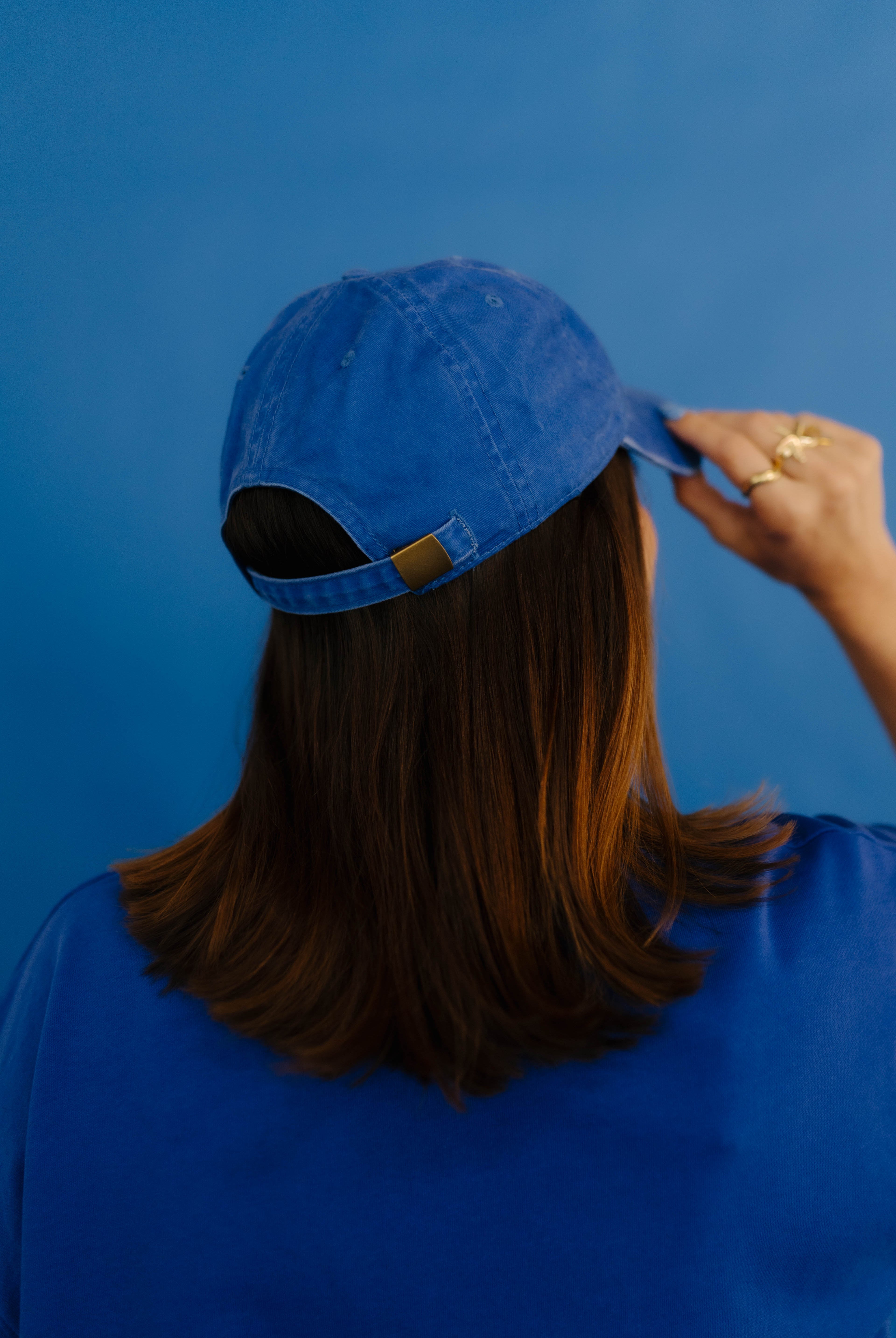Person wearing a blue cap against a blue background showing back of hat