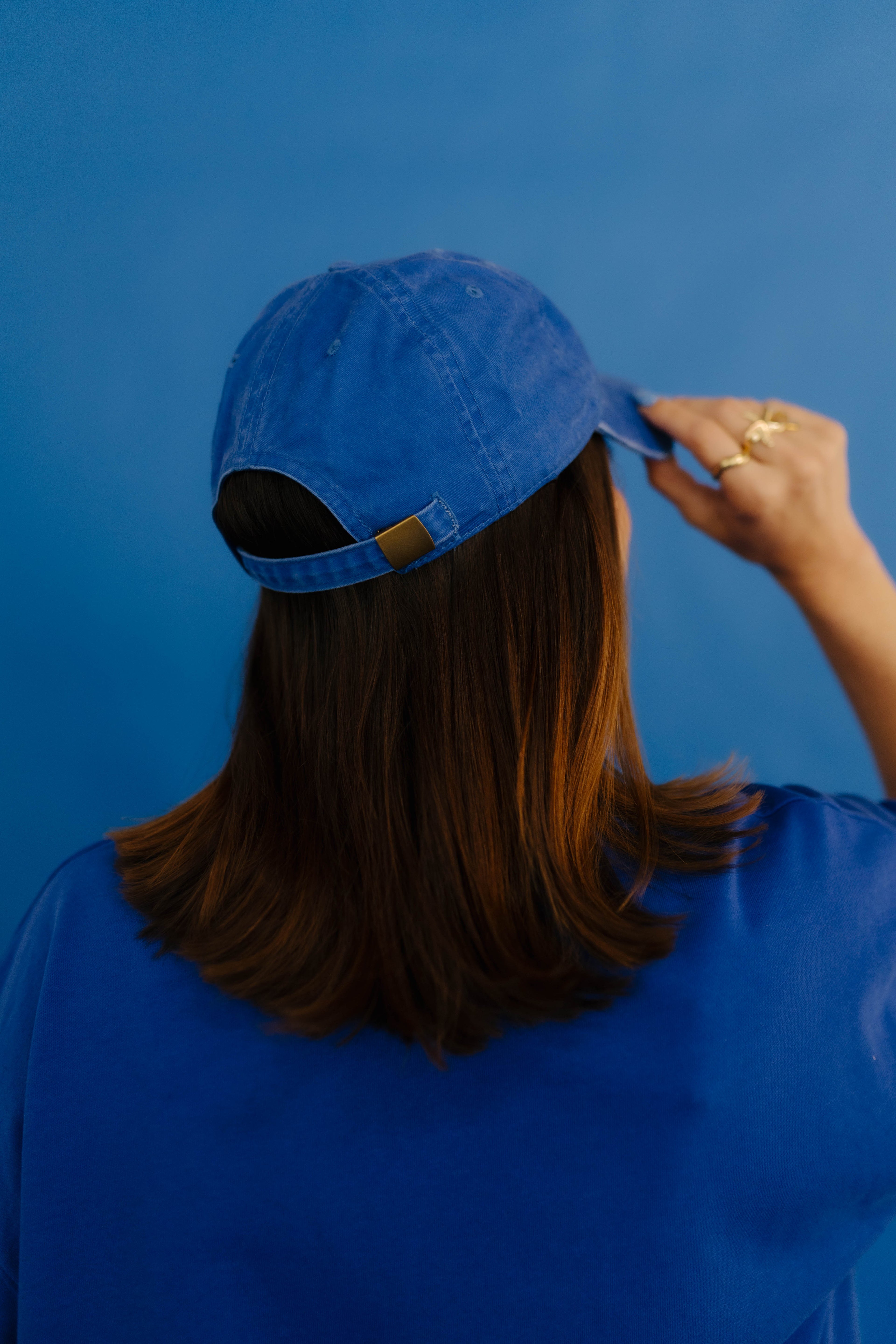 Person wearing a blue cap against a blue background showing back of hat