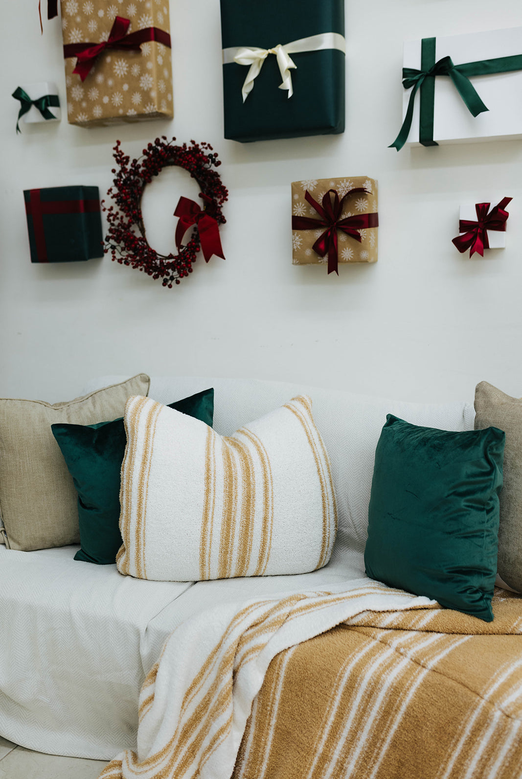 Decorative wall with Christmas-themed gift boxes and a wreath, featuring pillows and blankets on a couch.