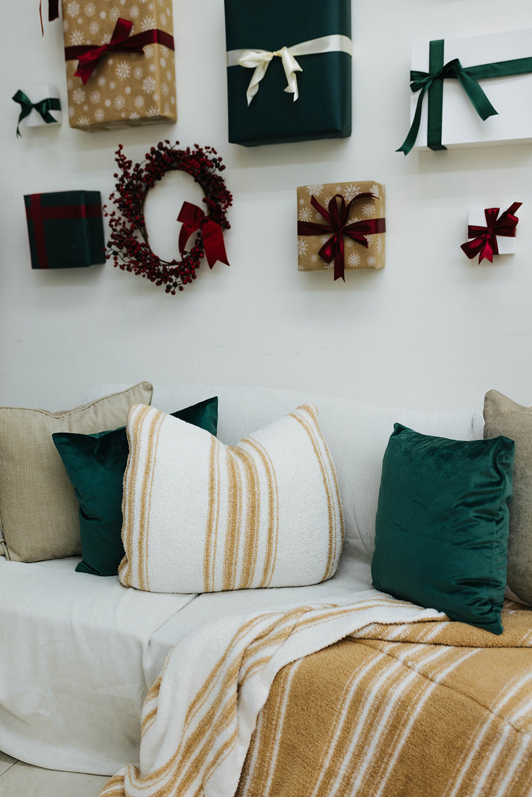 Decorative wall with Christmas-themed gift boxes and a wreath, featuring pillows and blankets on a couch.