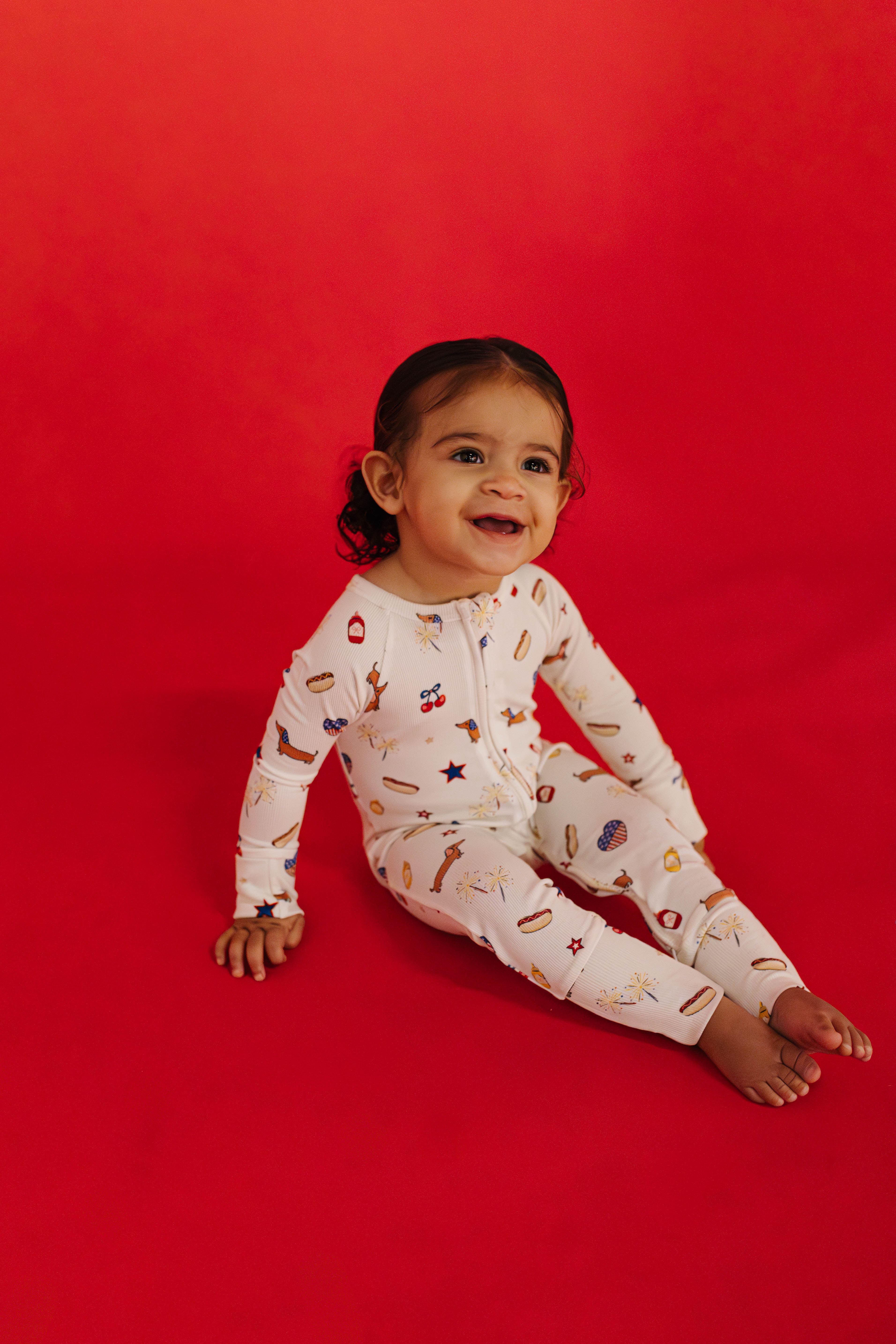 Child wearing a white onesie with colorful patterns on a red background