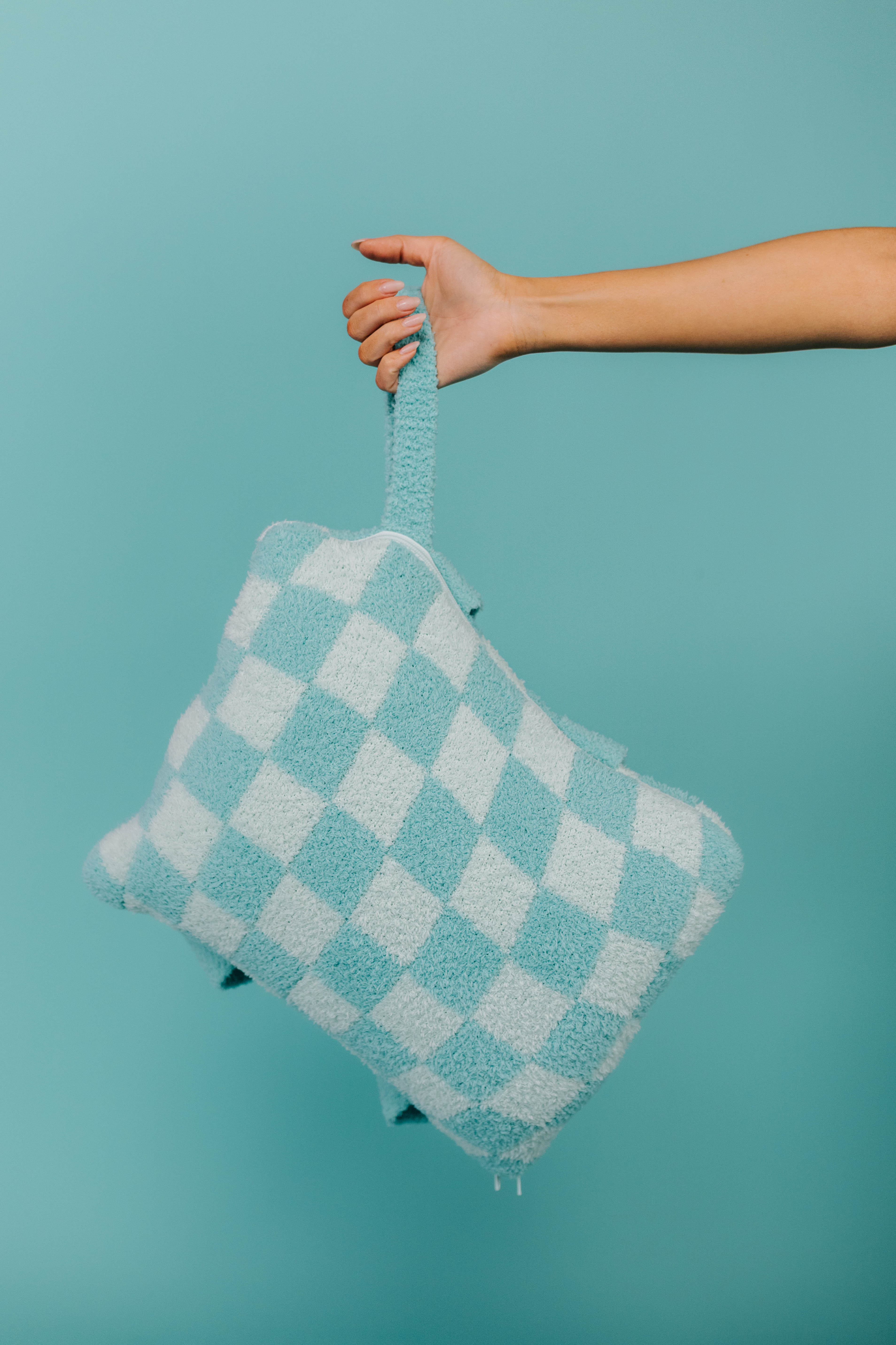 Hand holding a checkered quillow against a teal background