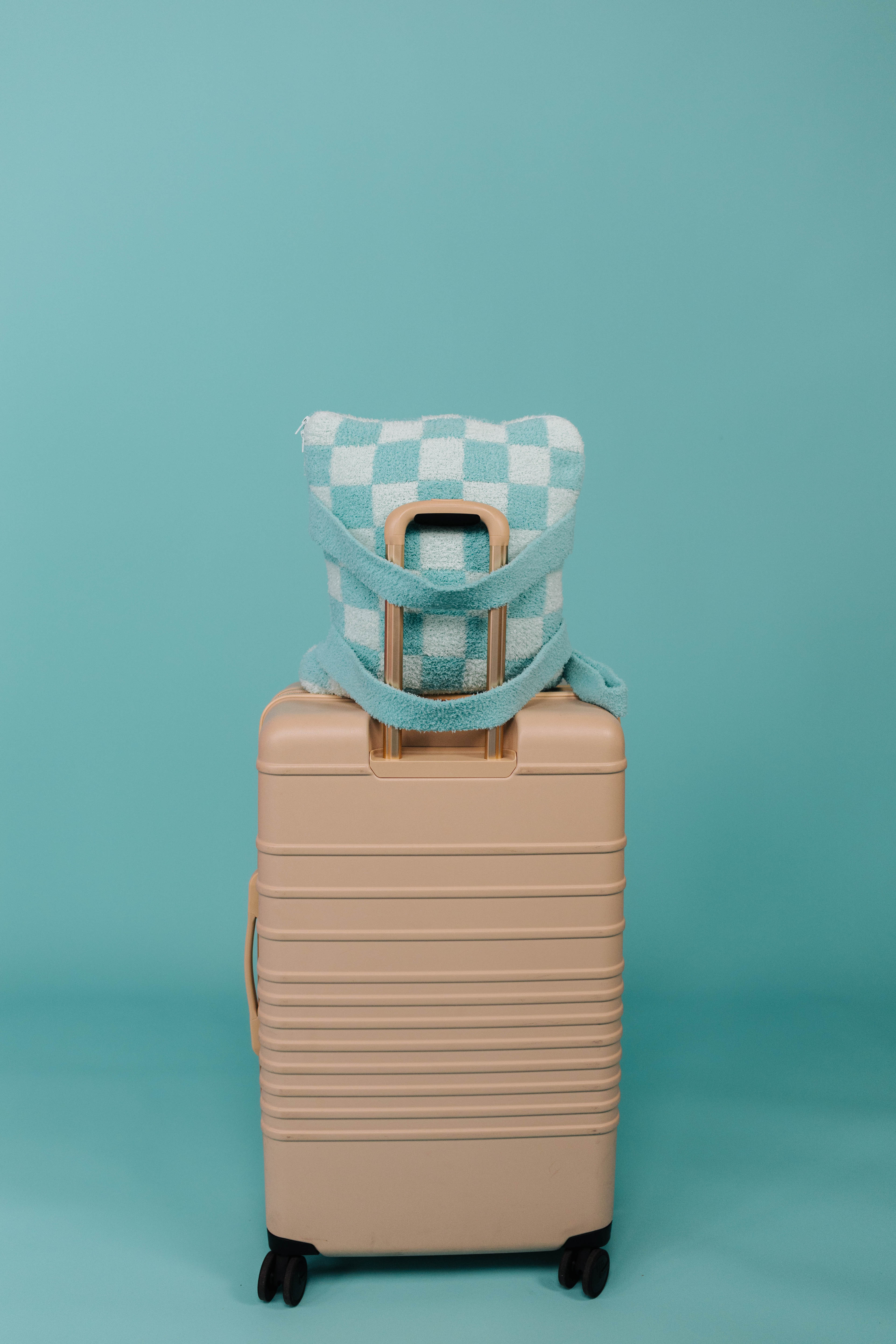 Beige suitcase with a checkered quillow on a teal background