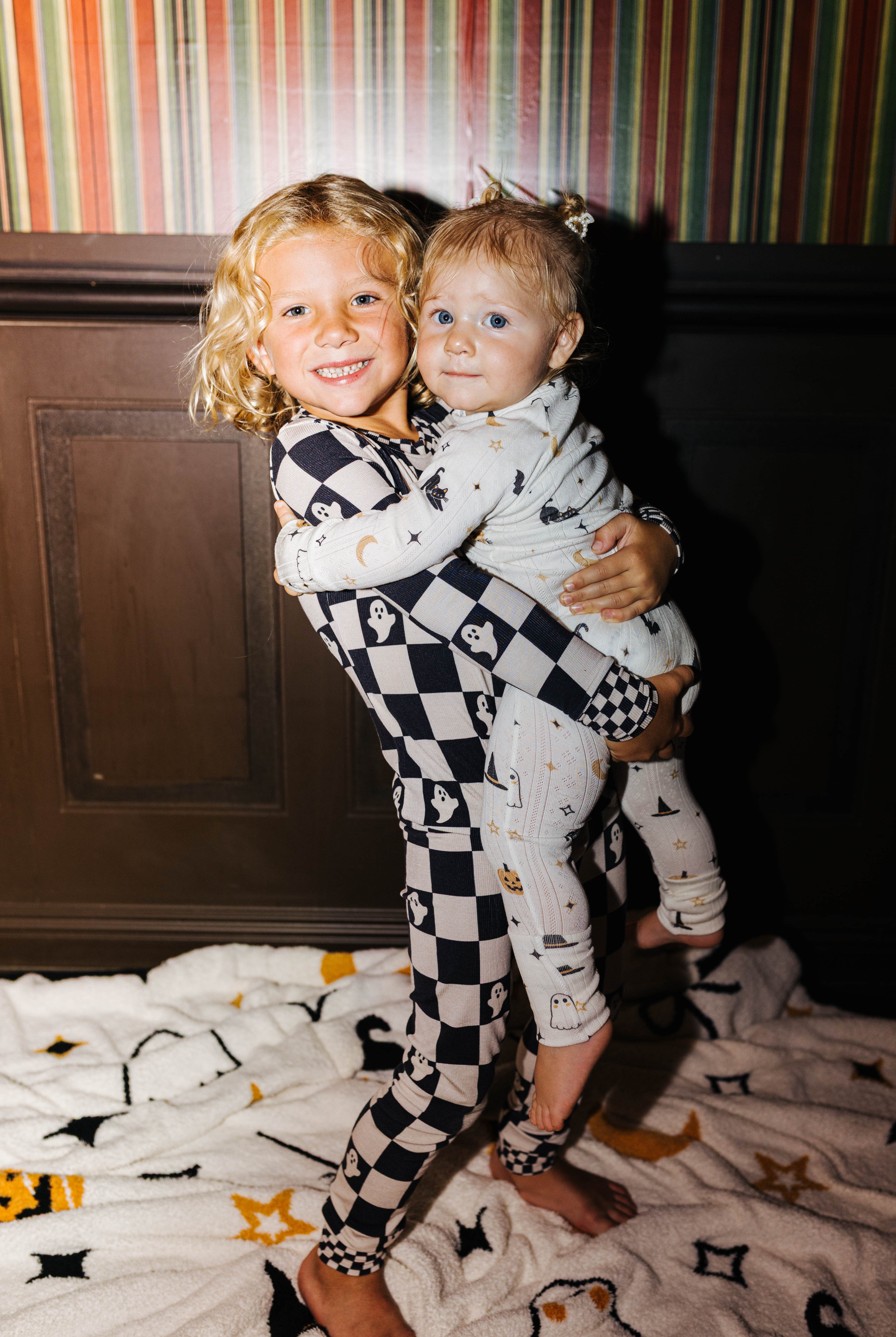 Two young children wearing halloween pjs one holding the other
