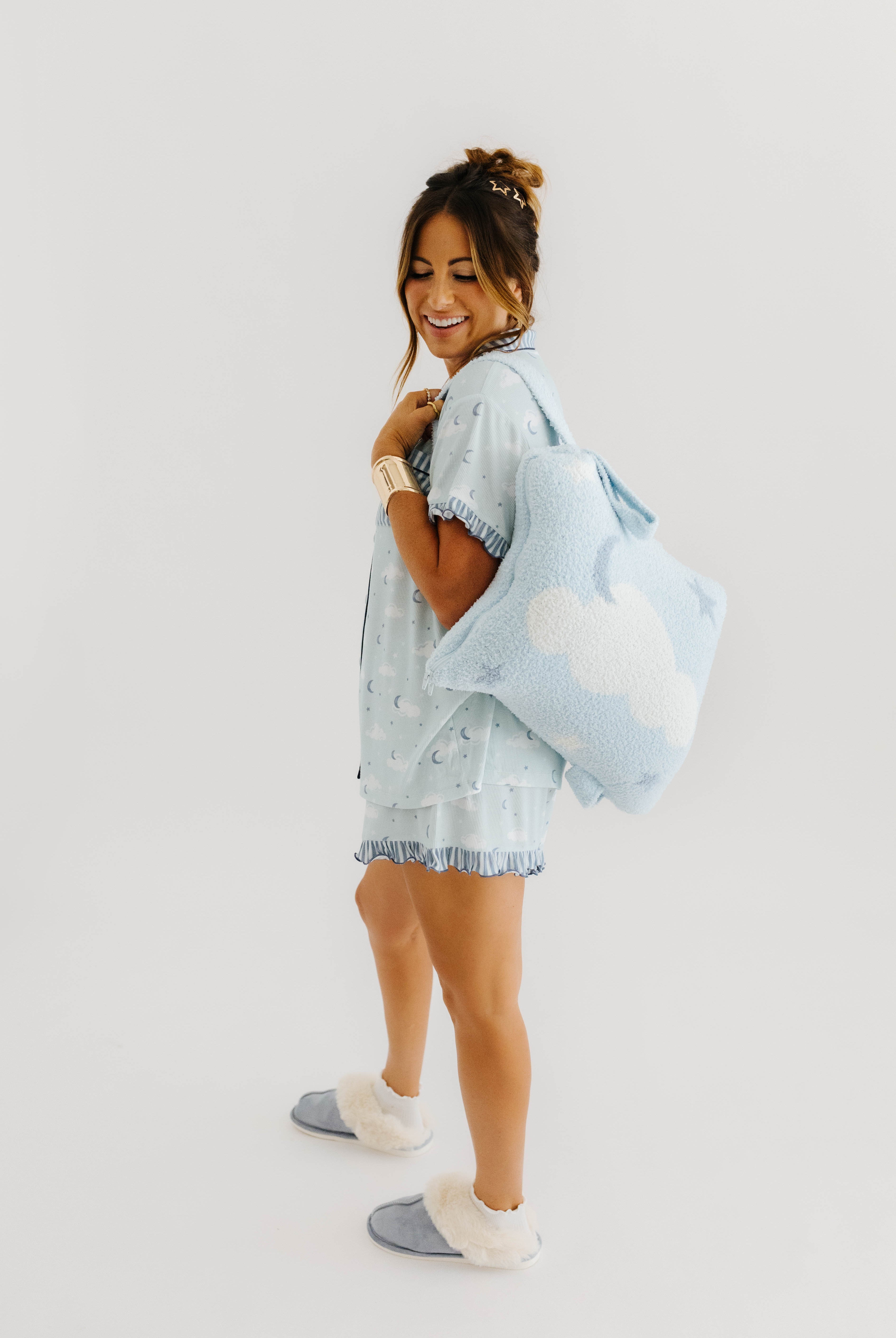 model krista wearing cloud ruffle pajamas and holding cloud backpack/wristlet quillow over shoulder