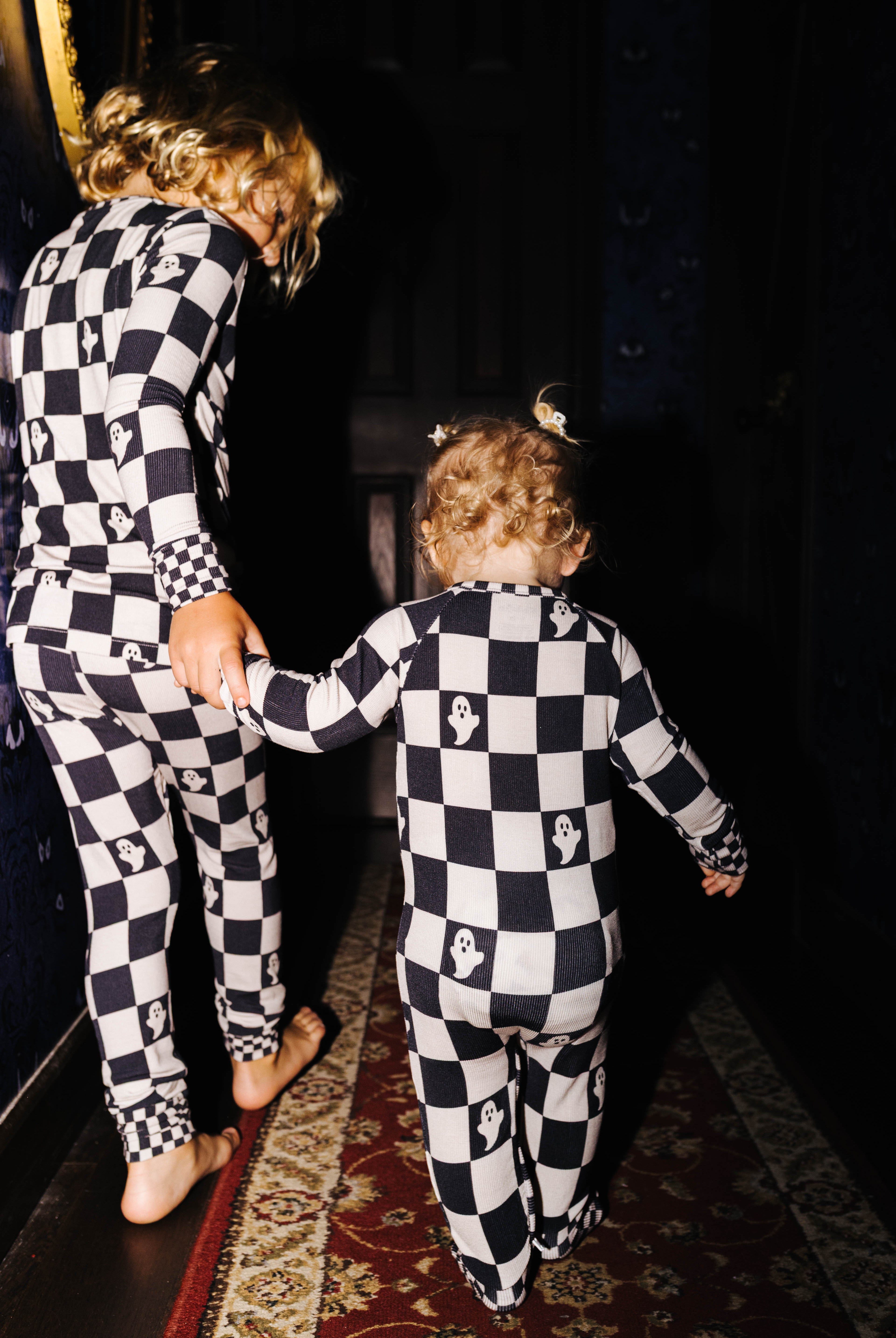 Back view of baby Ghost Check zip pajamas beside an older child