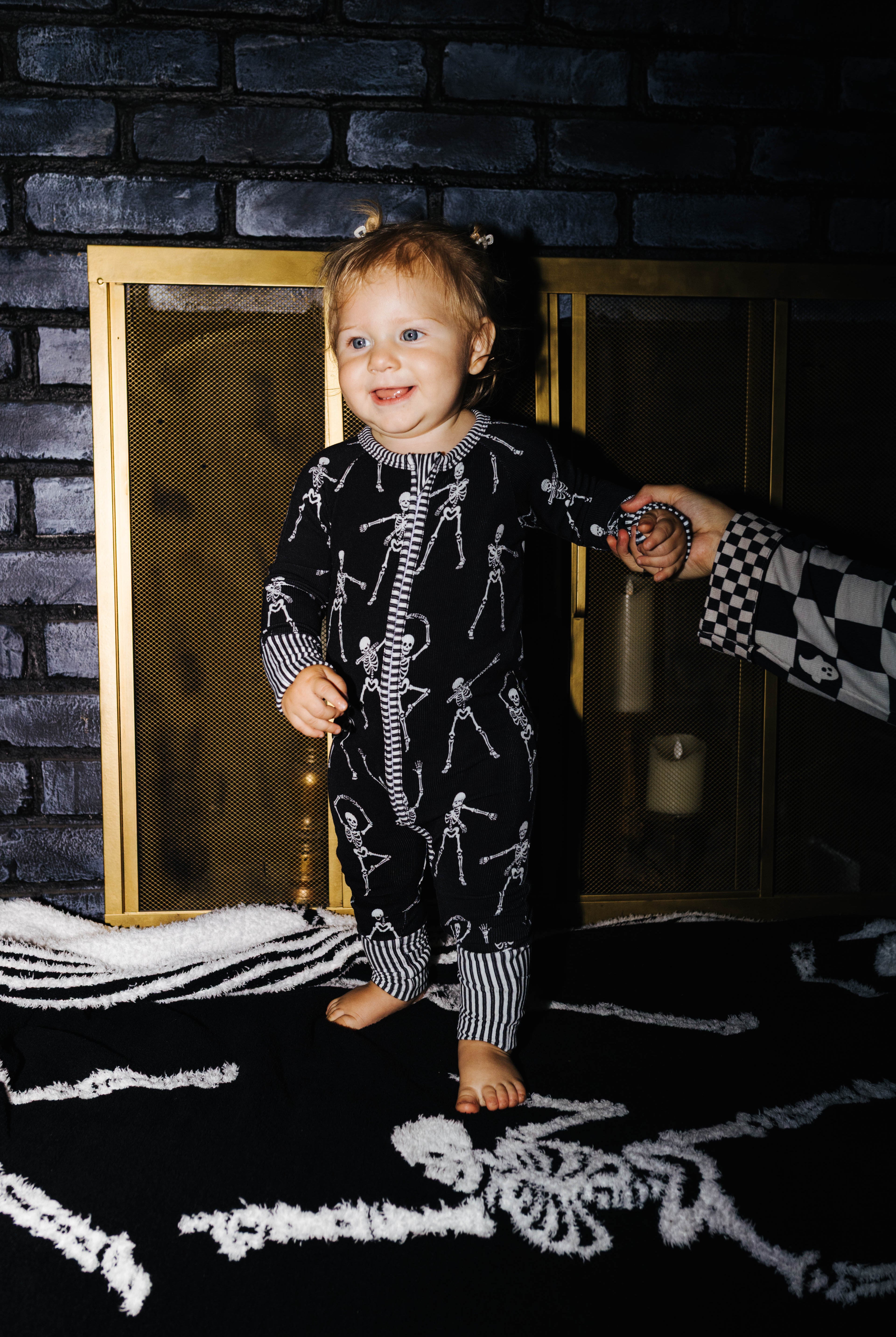 Baby wearing Skelly zip pajamas in front of a fireplace