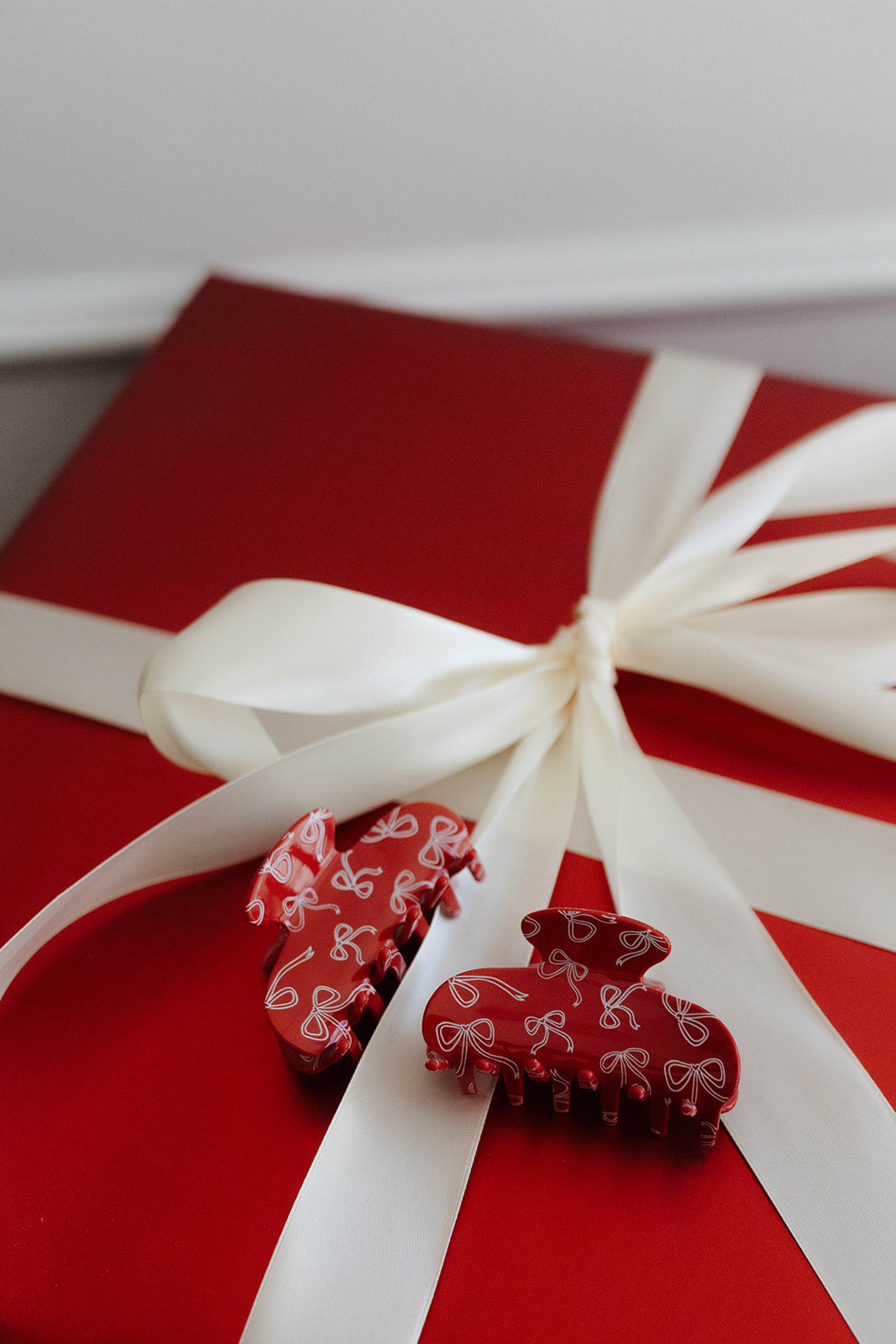 Red gift box with white ribbon and decorative red clips on a white background
