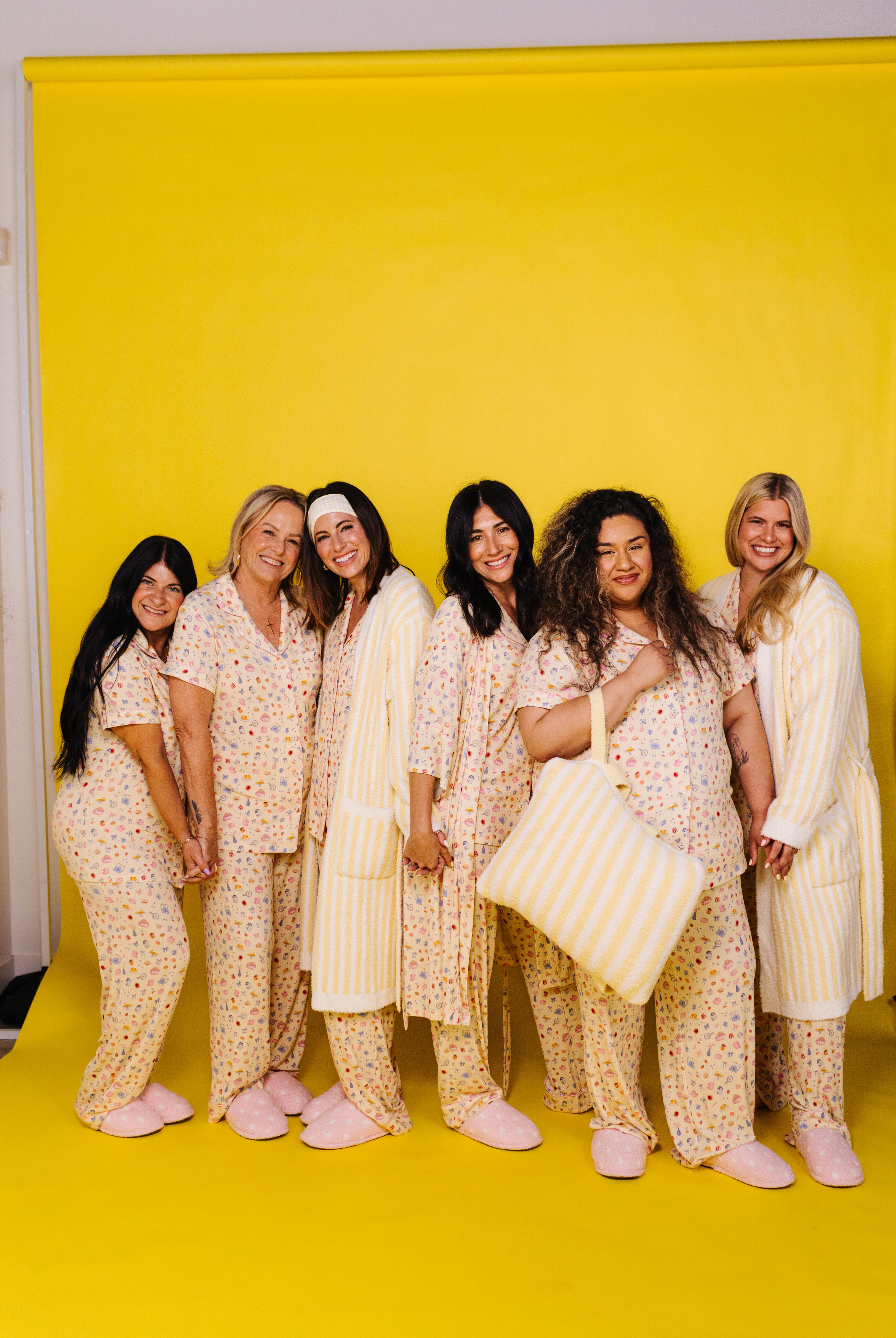 Group of women in matching pajama sets posing against a yellow backdrop
