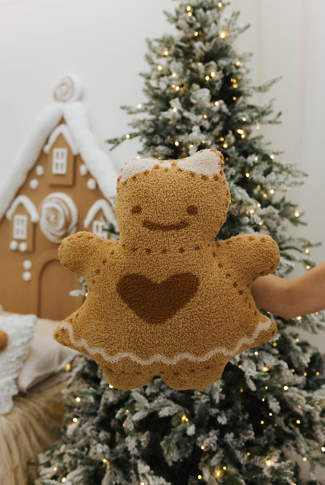 Gingerbread-shaped plush toy held in front of a decorated Christmas tree.