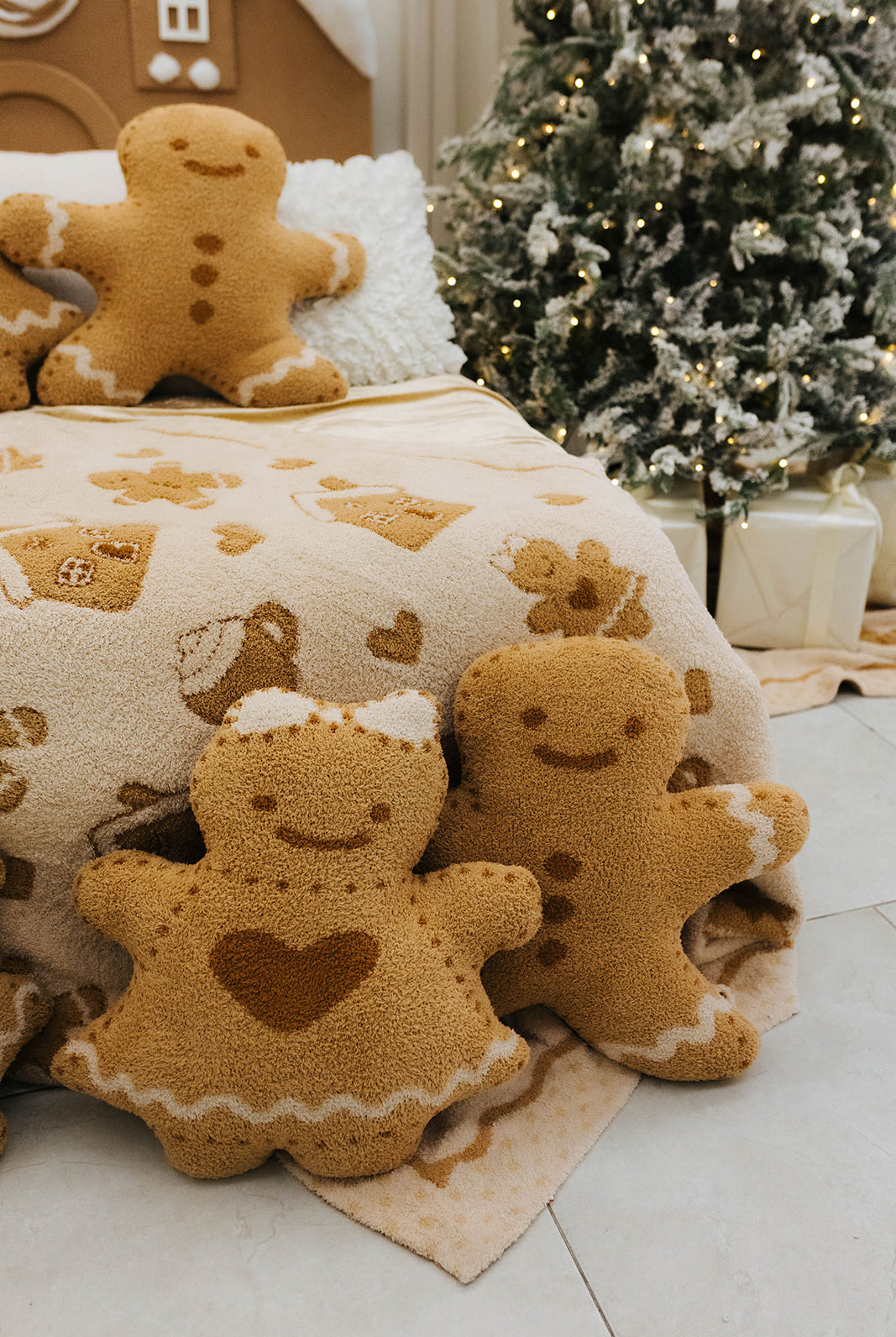 Gingerbread-themed plush toys on a decorative blanket with a Christmas tree in the background.