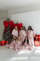 Group of women in matching pajamas posing in front of a Christmas tree with large red bows and presents.