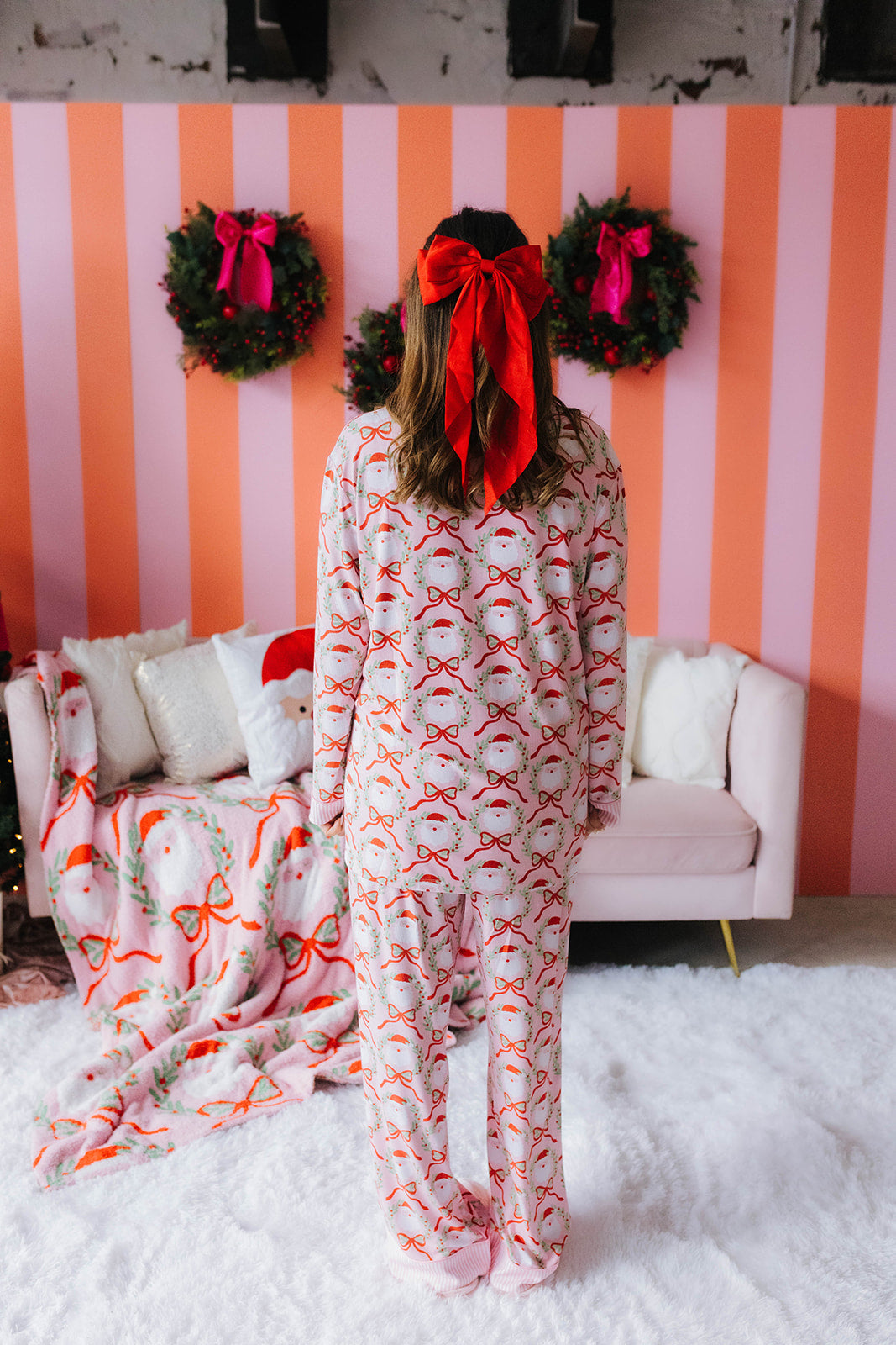 Person wearing festive pajamas with a striped wall and wreaths in the background