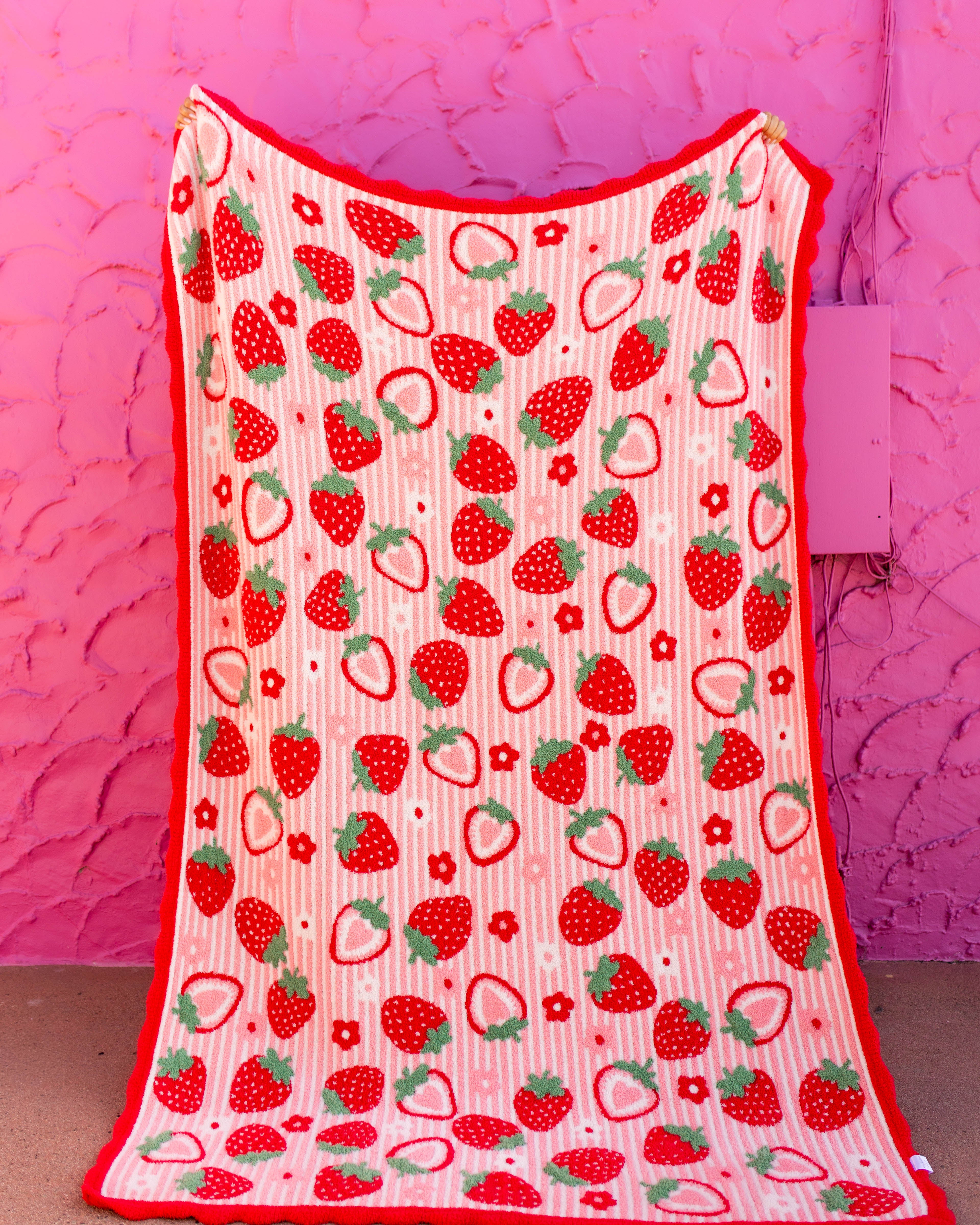 front of strawberry blanket with red scallop edged being held against a pink wall