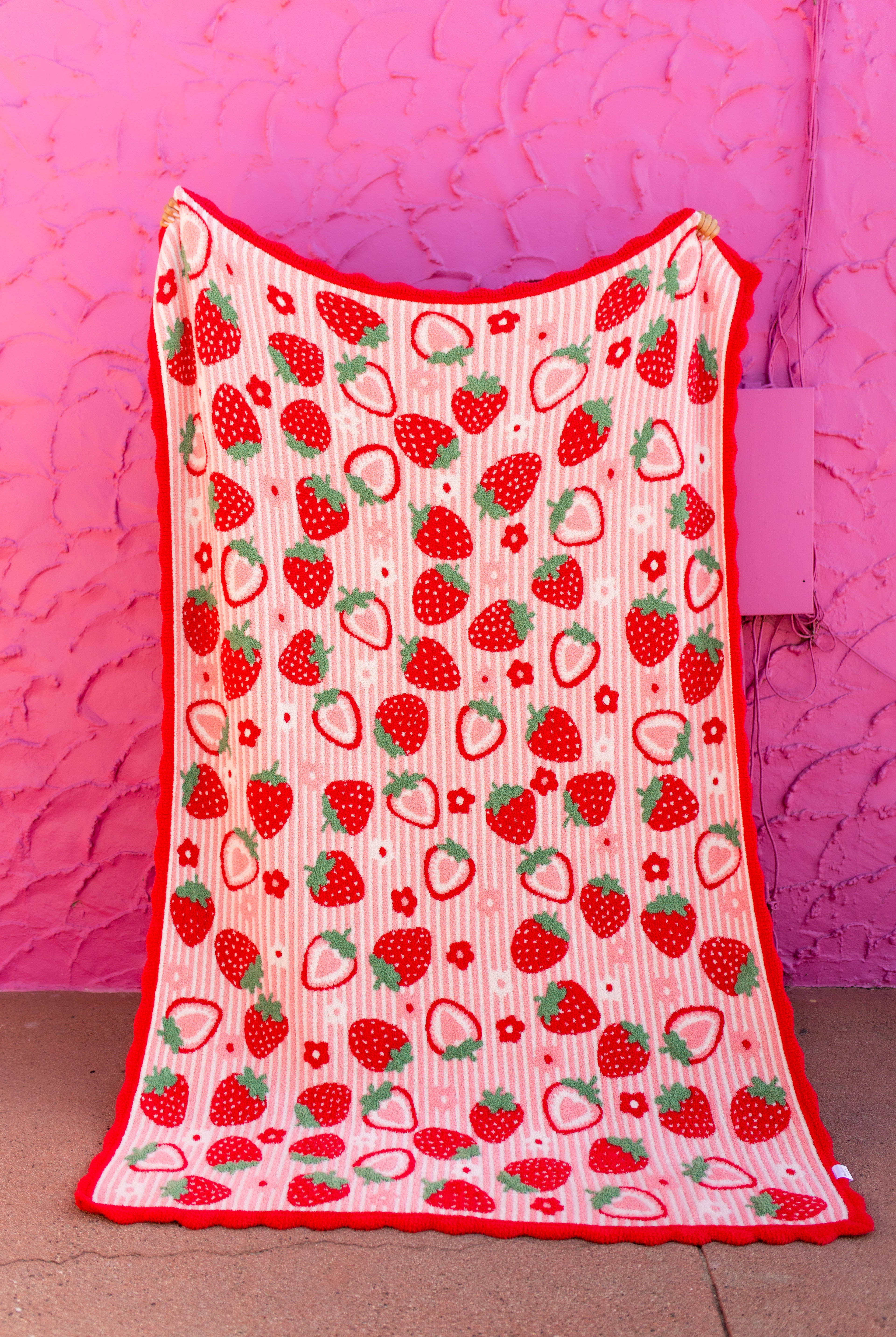 front of strawberry blanket with red scallop edged being held against a pink wall
