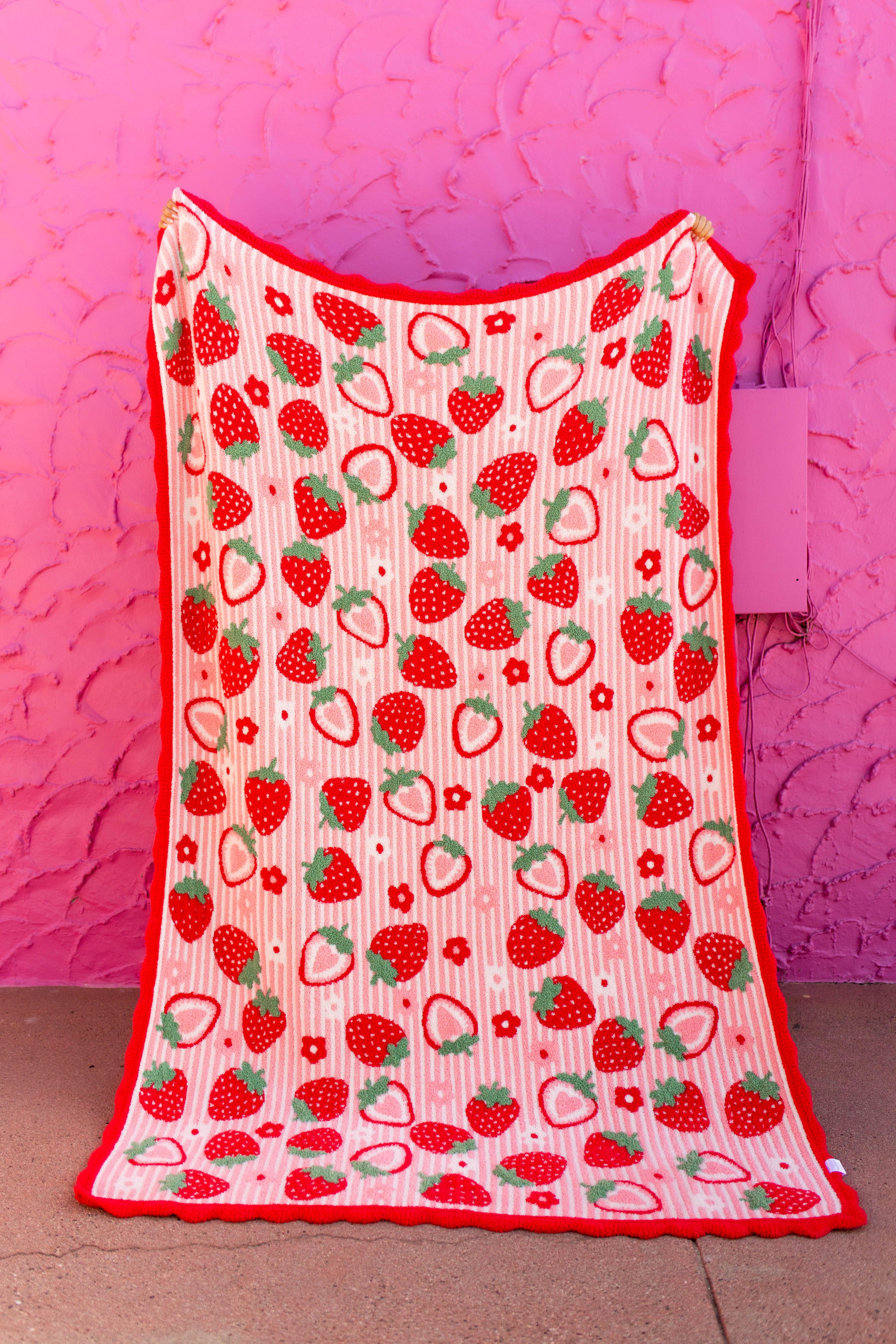 front of strawberry blanket with red scallop edged being held against a pink wall