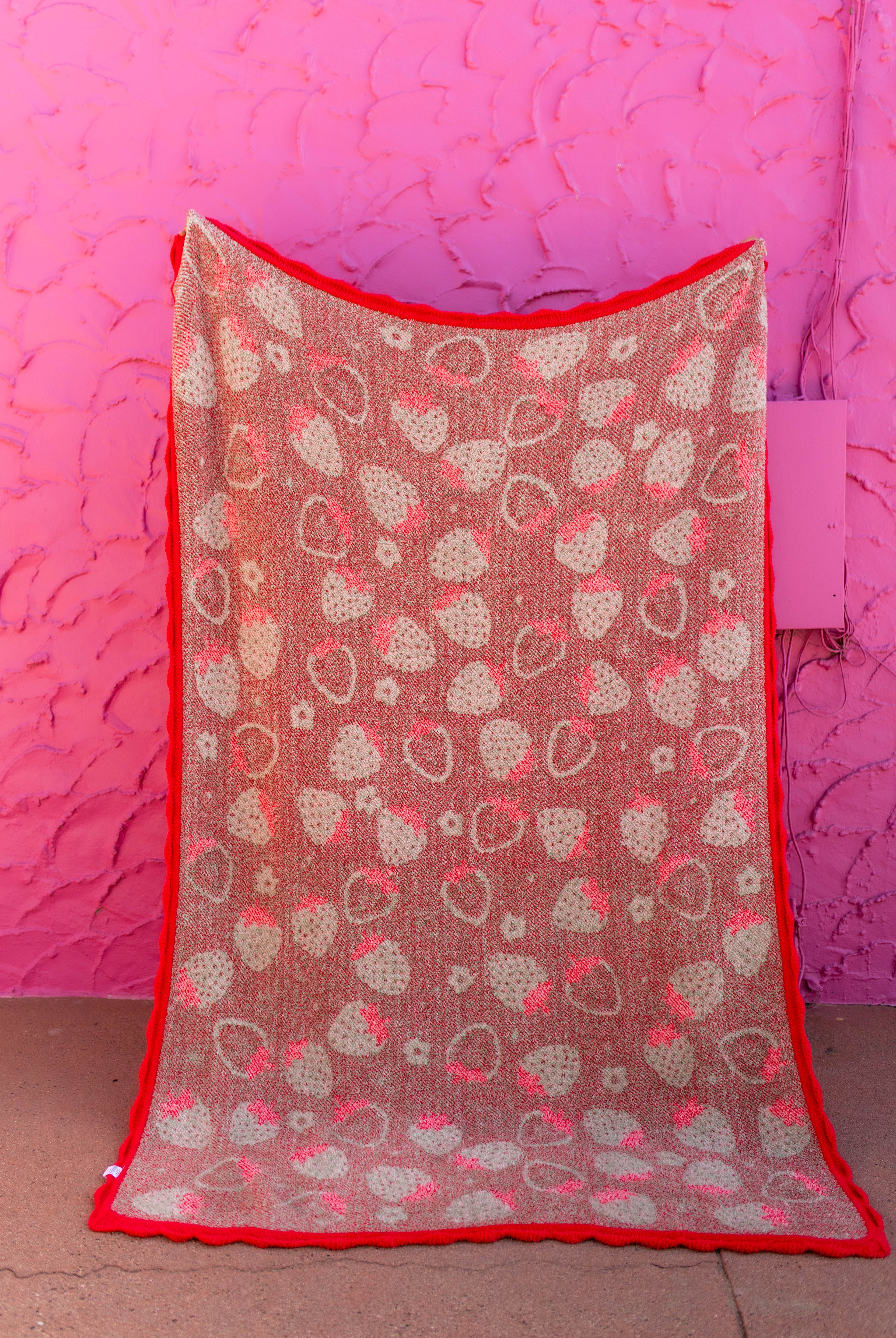 Back of the strawberry blanket showing the mostly red/green print held against a pink background