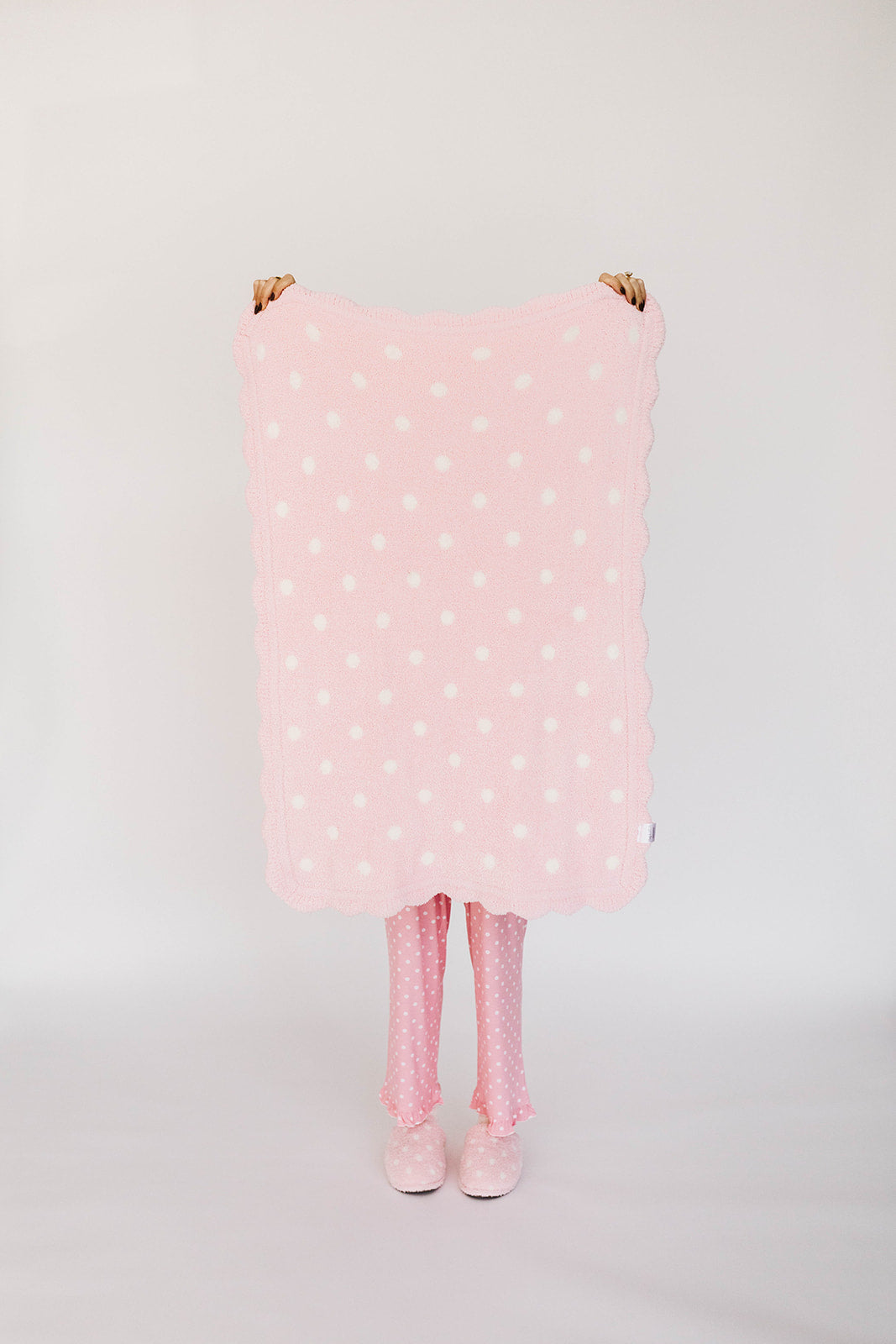 Person holding a pink polka dot blanket with a white background
