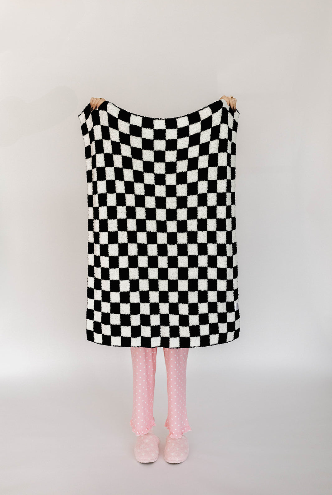 Person holding a black and white checkered blanket on a plain background