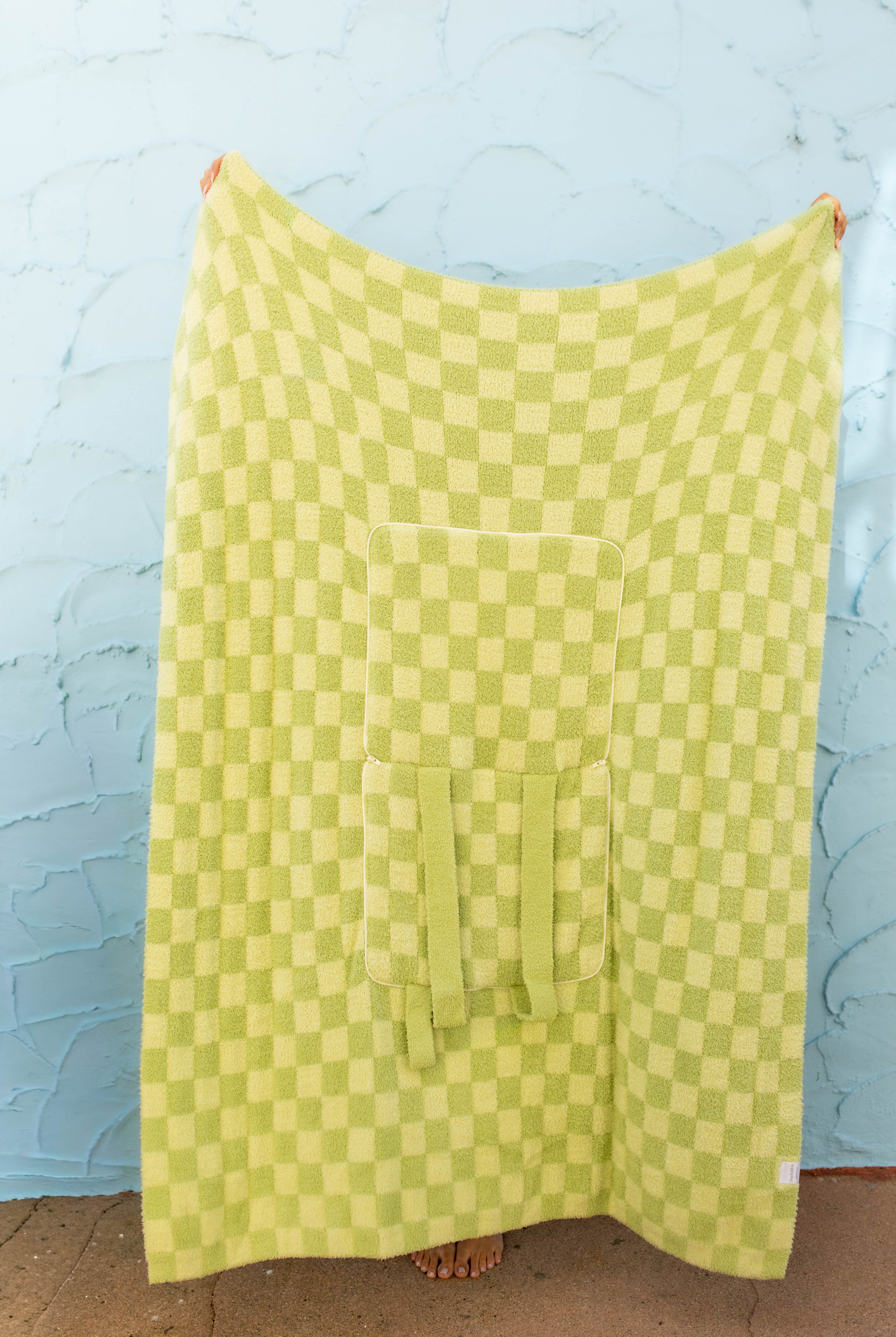 Front of the green check quillow , hanging against a light blue textured wall.
