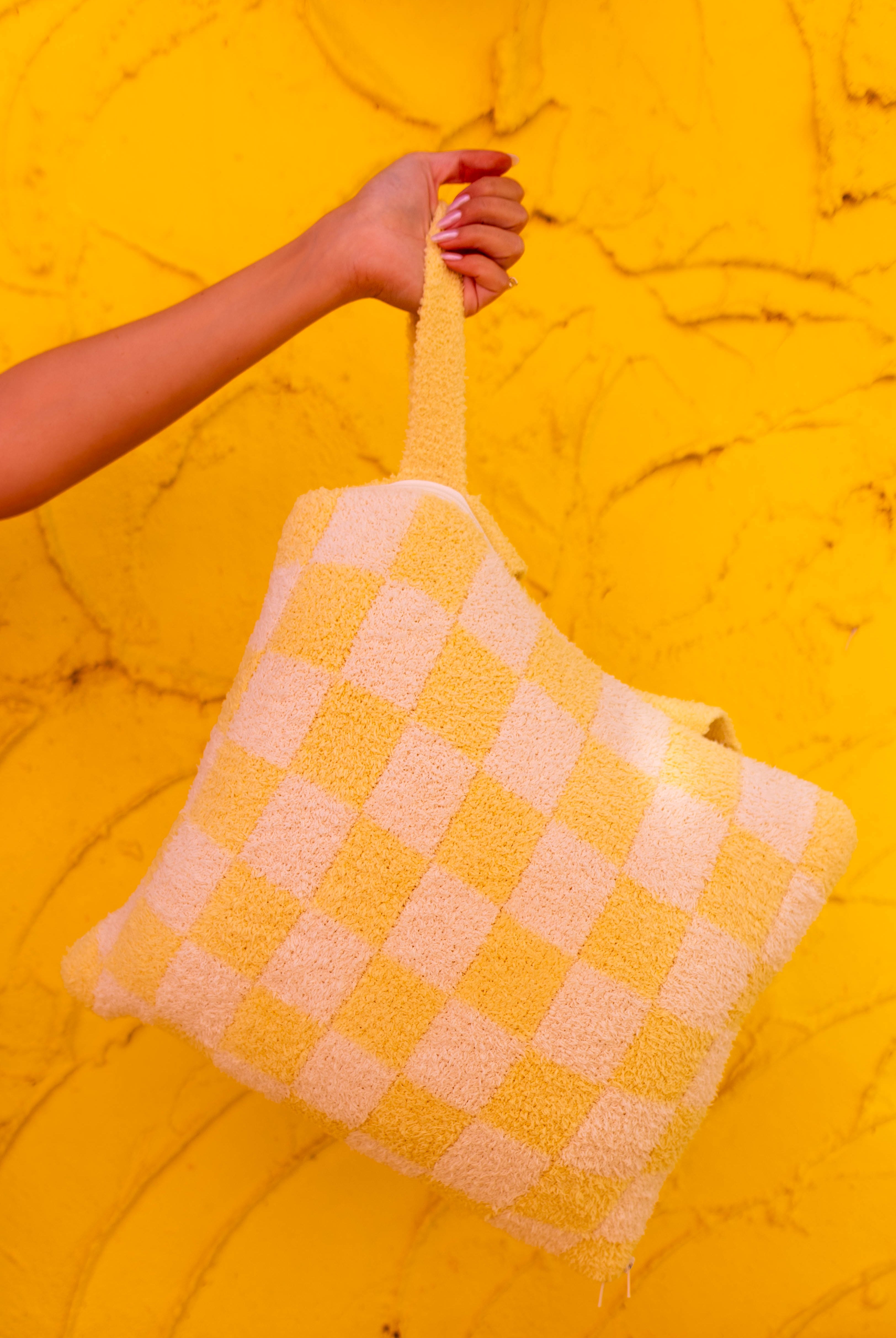 A knit check quillow held by a person's hand against a bright yellow textured background.