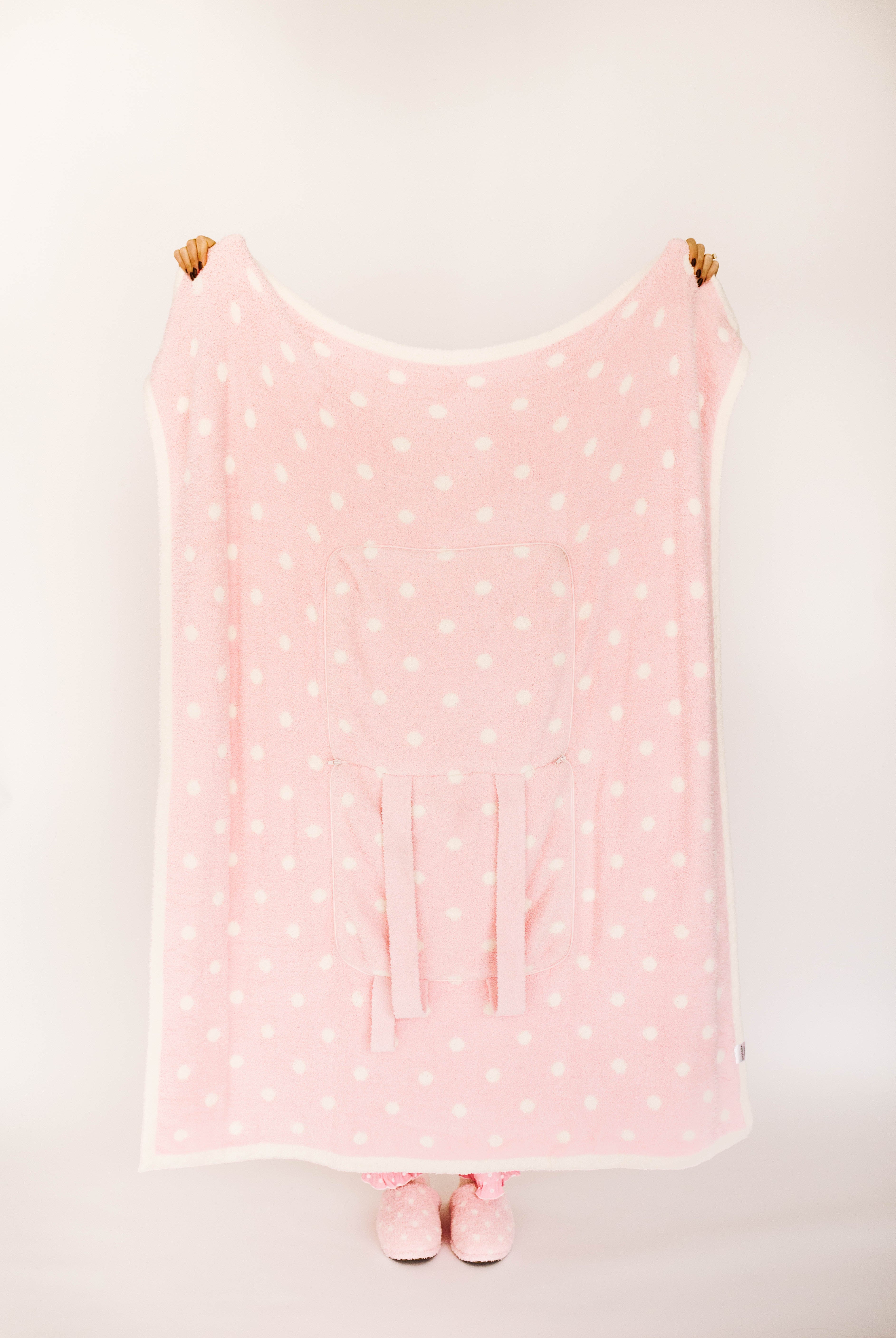 Pink polka dot blanket with matching slippers on a white background