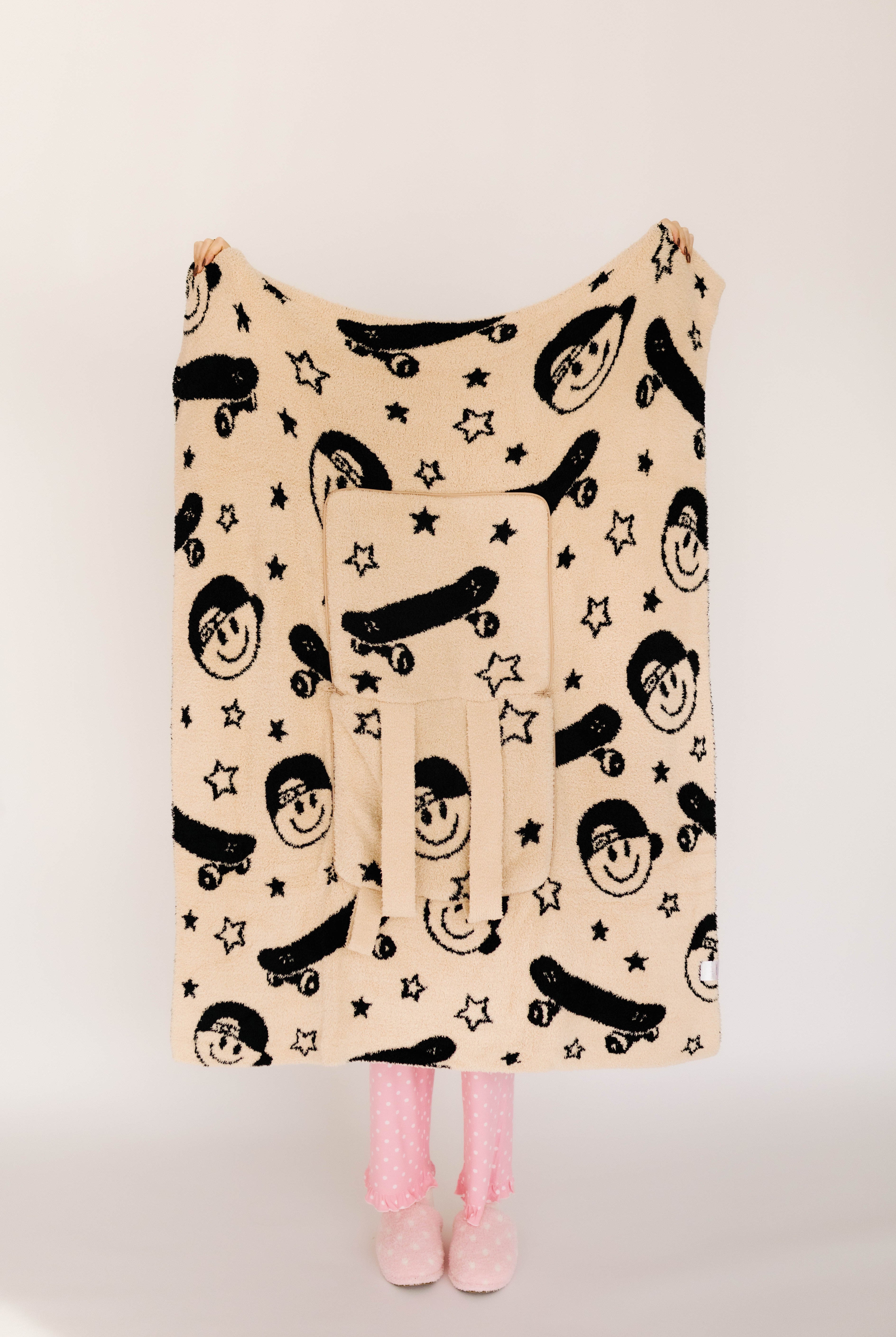 Beige blanket with black smiley and skateboard pattern on a plain background