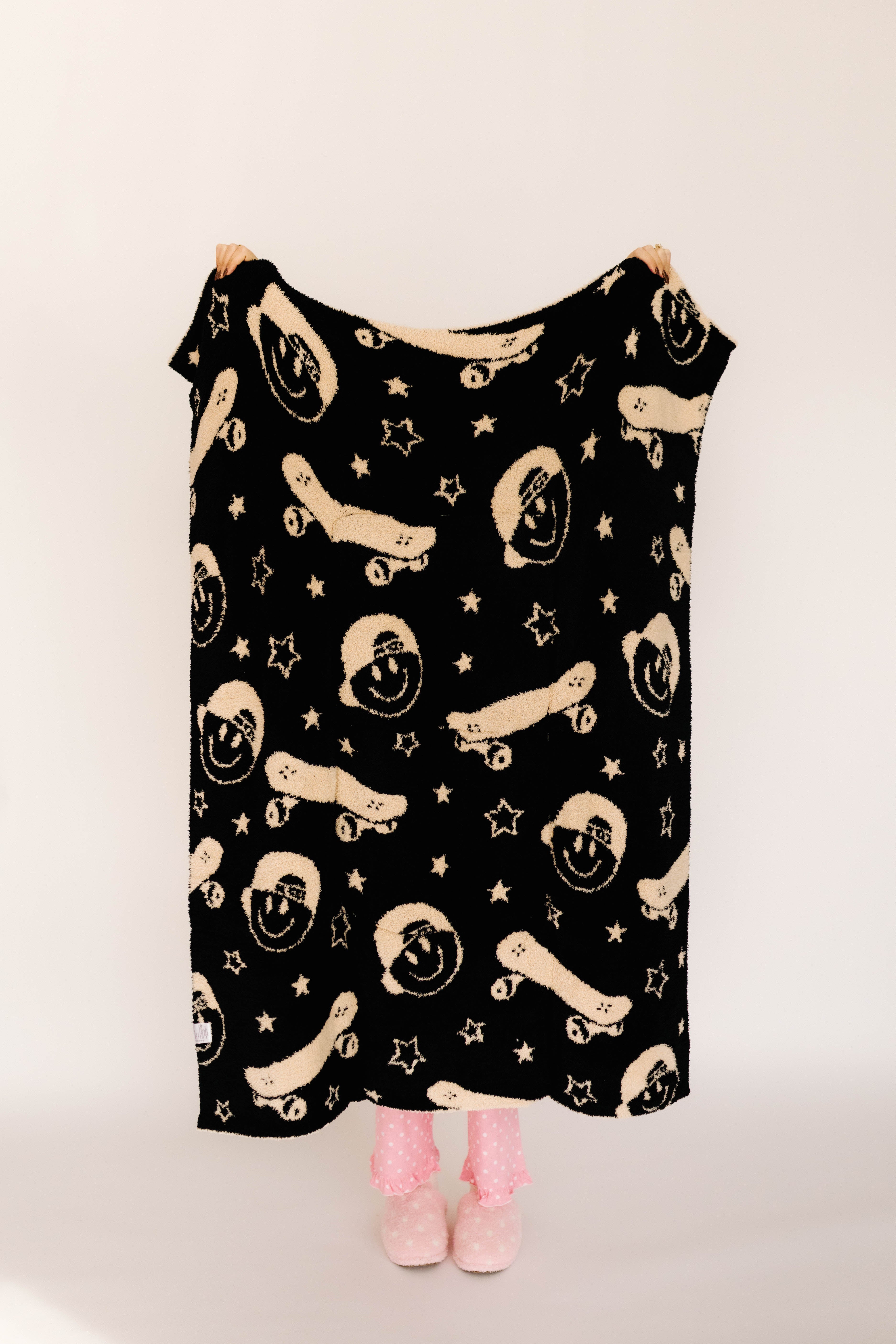 Black blanket with beige skateboards and smiley faces on a plain background
