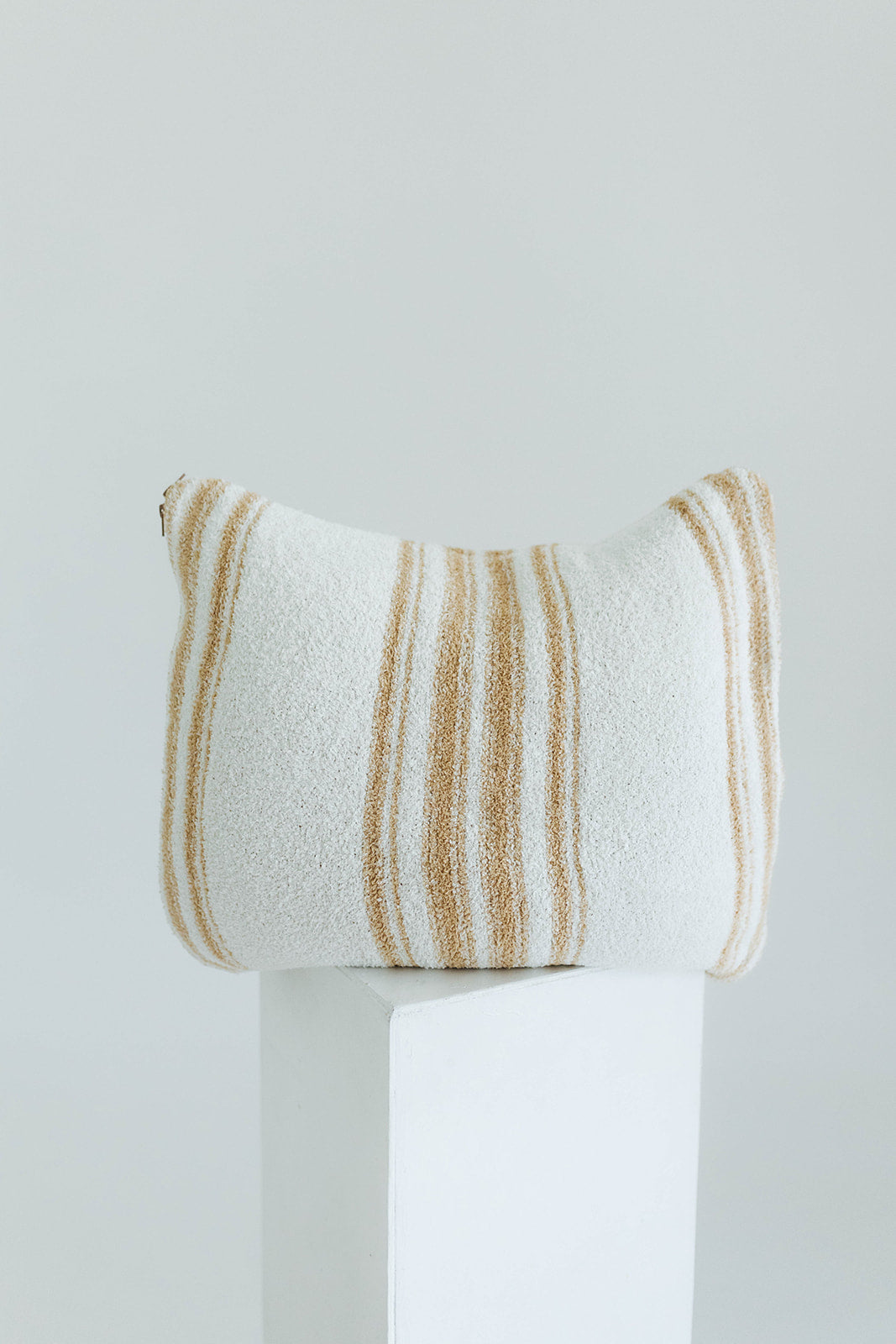 Striped pillow on a white pedestal against a light gray background