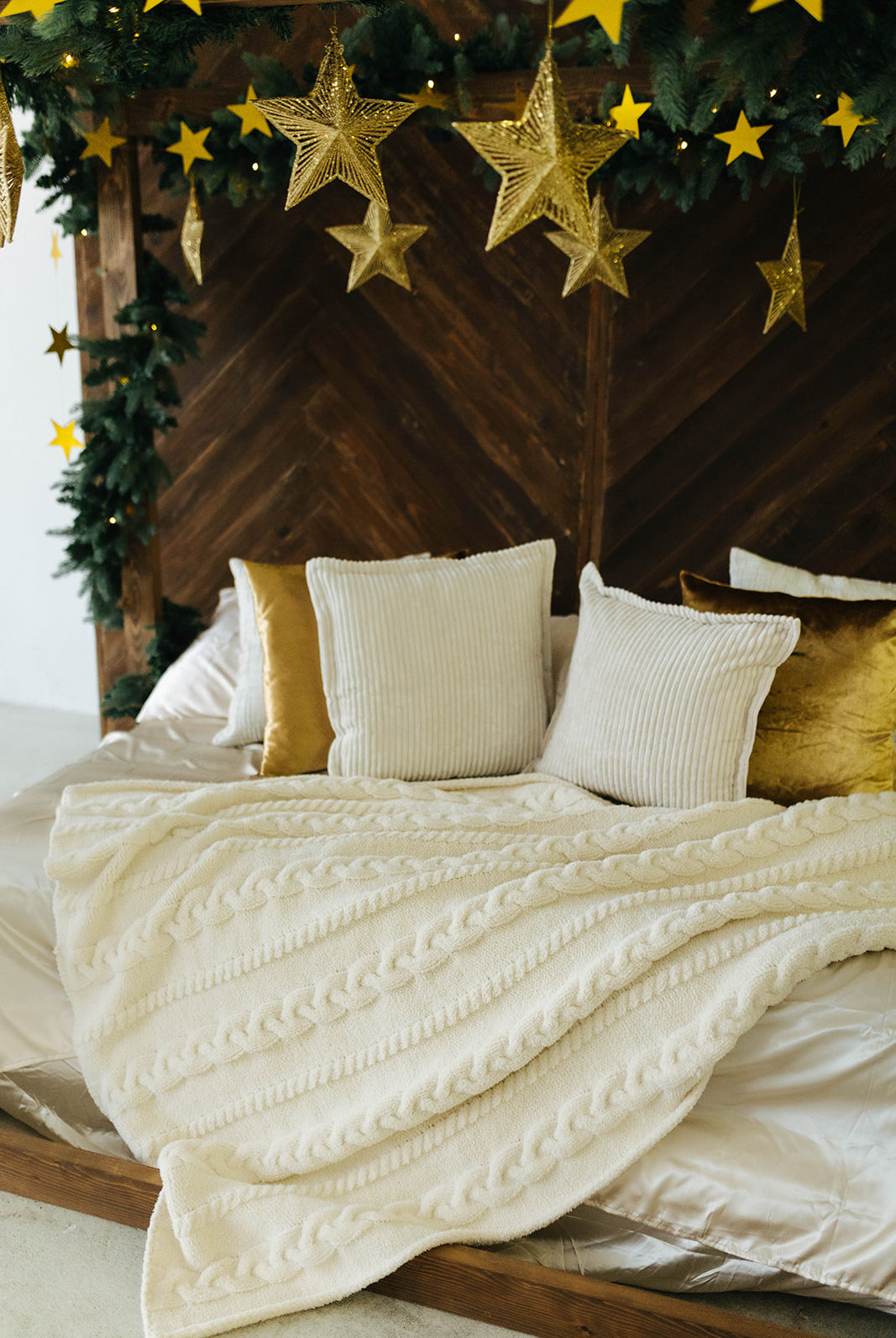 Decorative bed with white bedding and gold pillows, surrounded by Christmas decorations including stars and greenery.