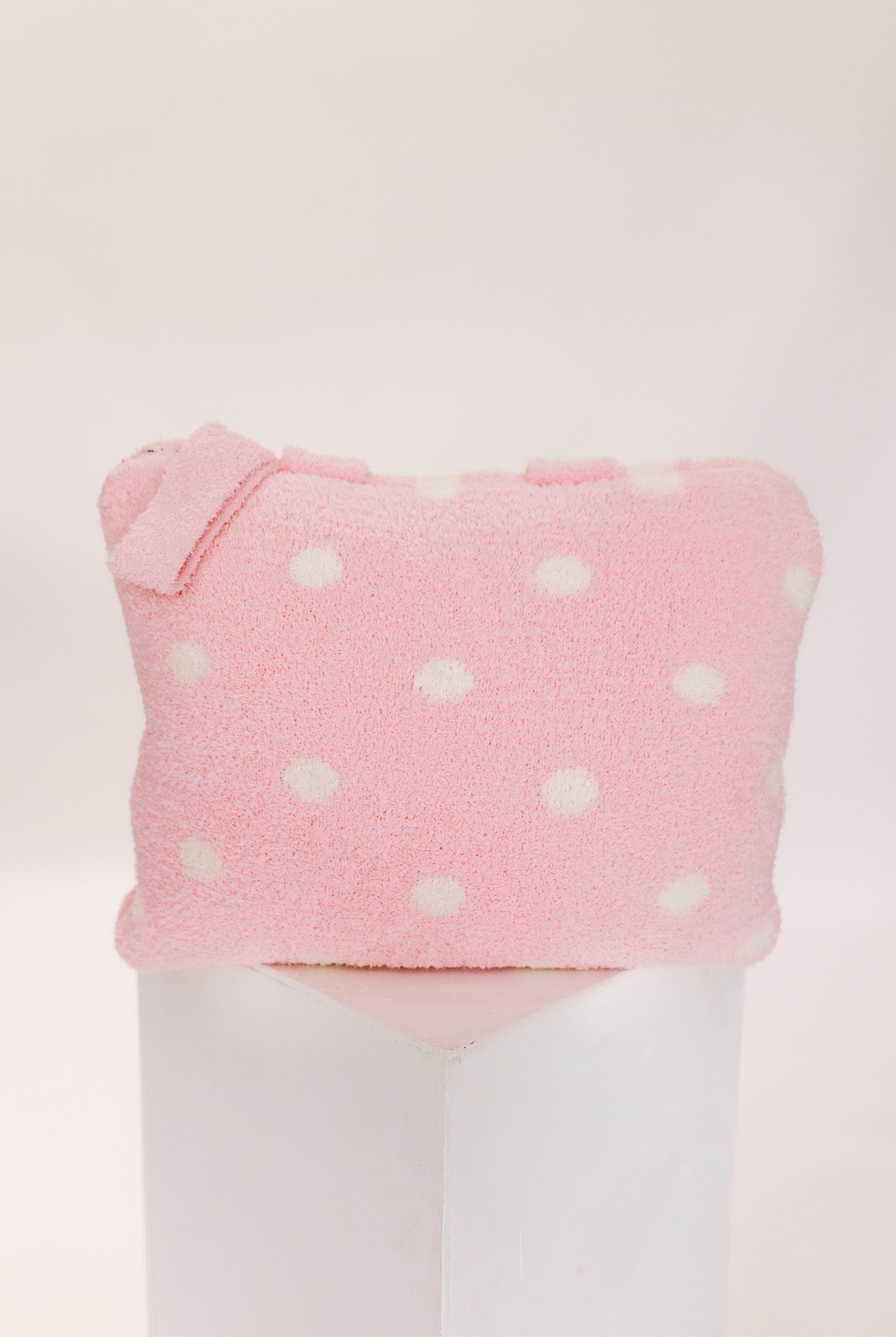 Pink polka dot pillow on a pillar against a white background
