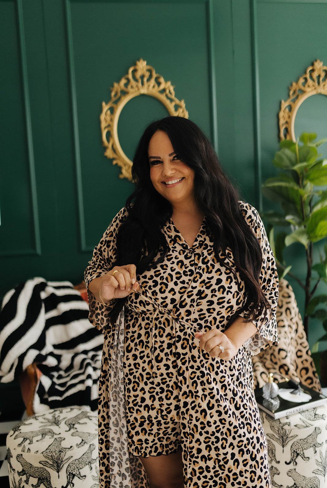 Woman in a leopard print outfit standing in a room with green walls and decorative mirrors.