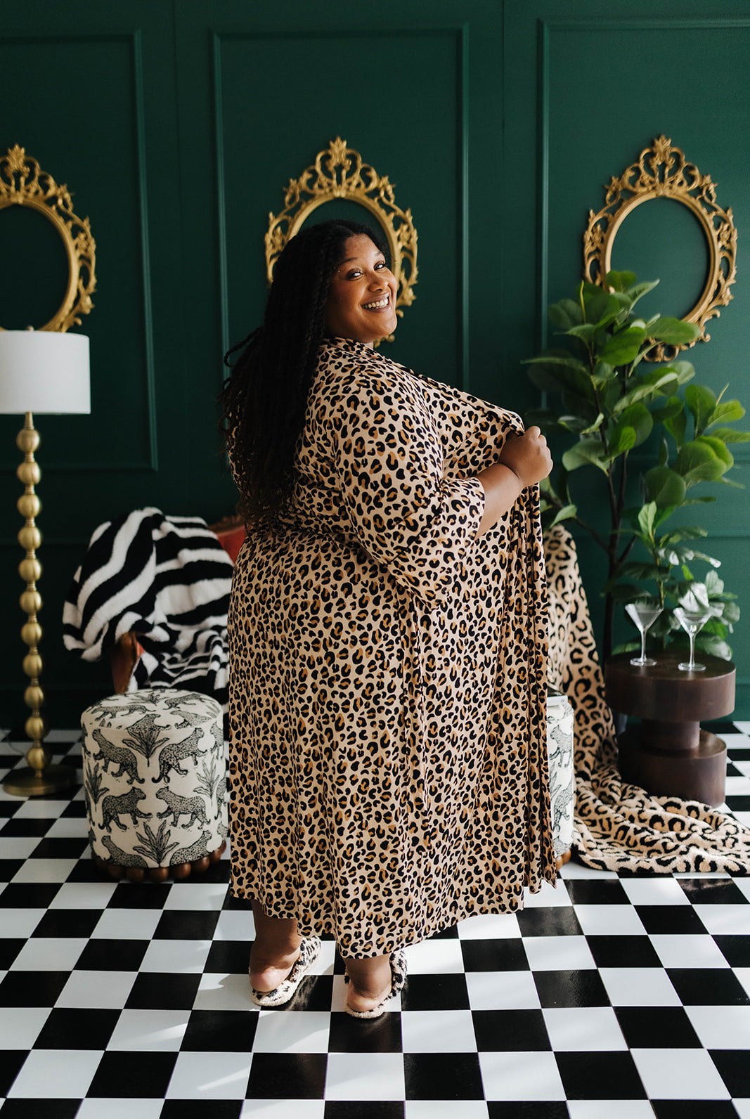 Woman in a leopard print outfit standing in a room with decorative mirrors and plants.