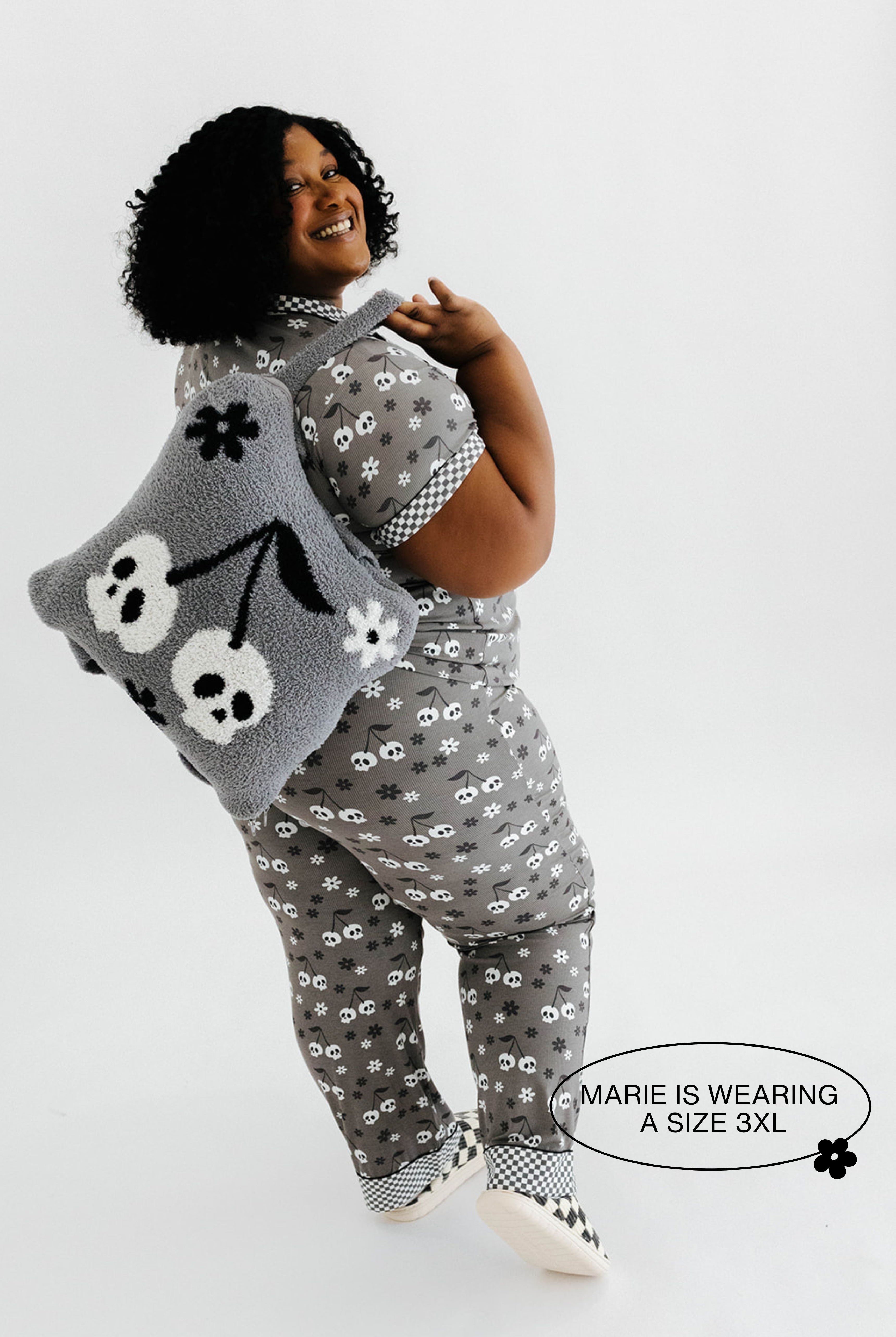 model mari wearing a size 3x in the skeleton pajamas holding the skeleton backpack and wristlet quillow over shoulder