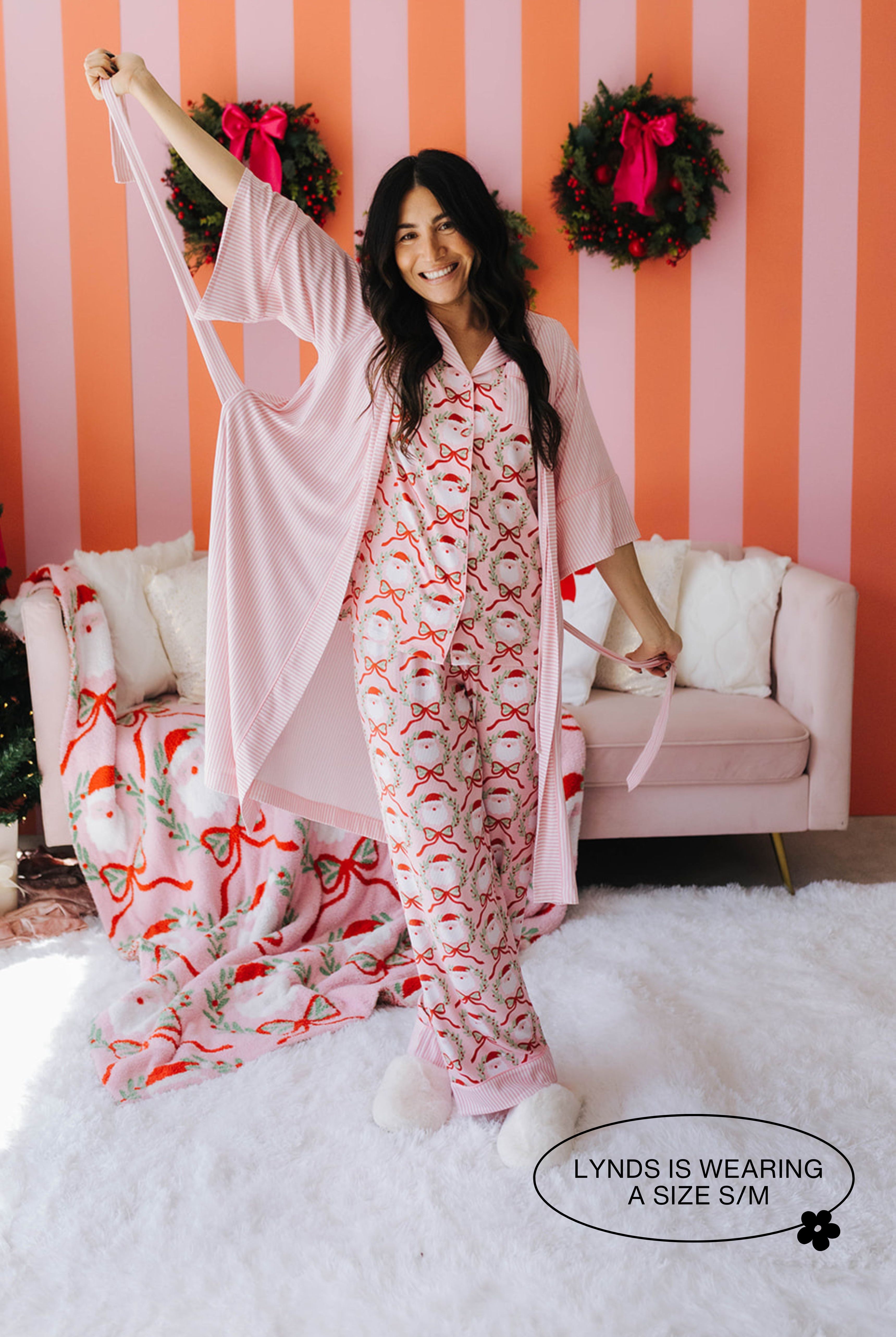 Woman in a pink and red patterned pajama set with a matching robe in a living room setting.
