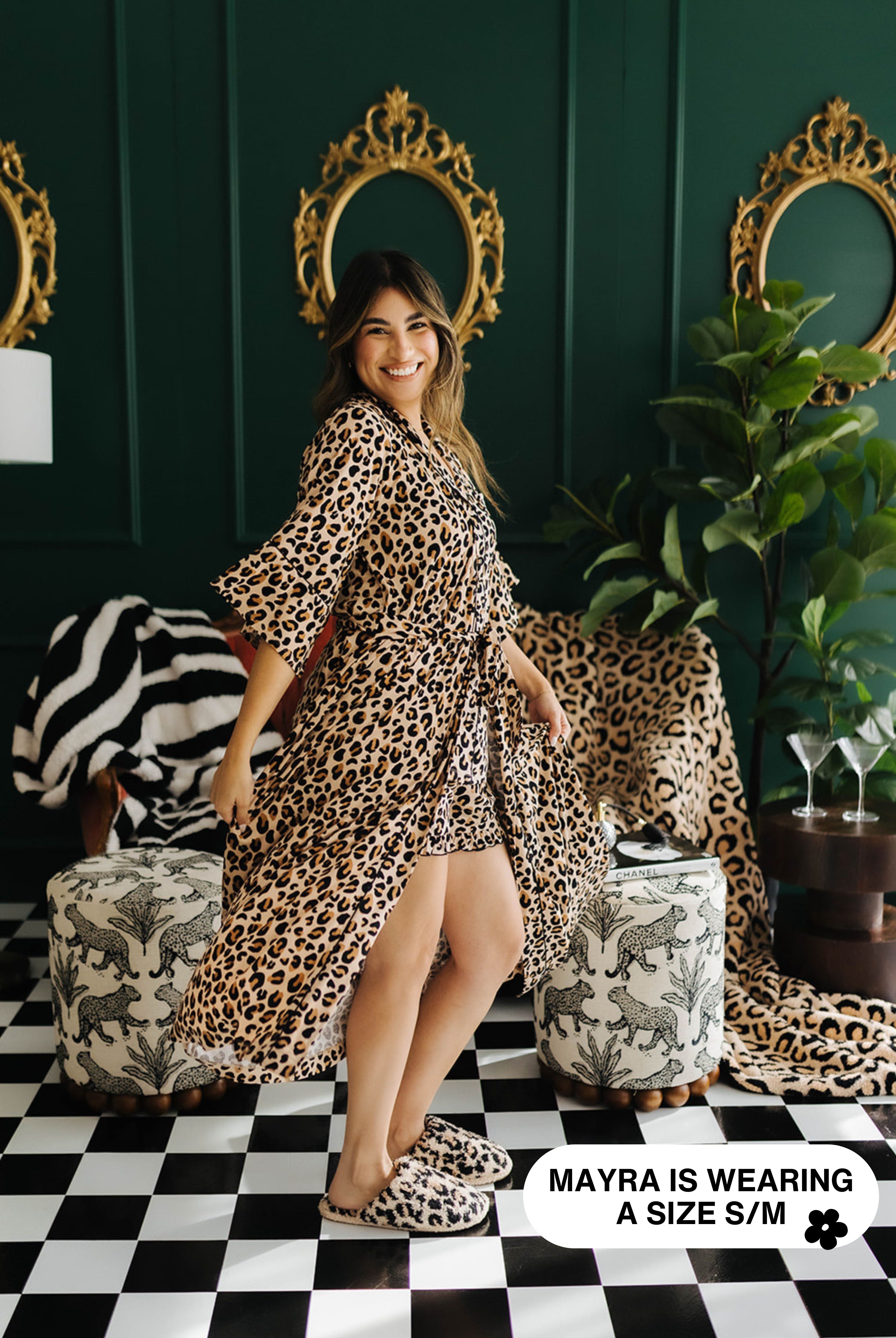 Woman wearing a leopard print robe in a stylish room with mirrors and plants.
