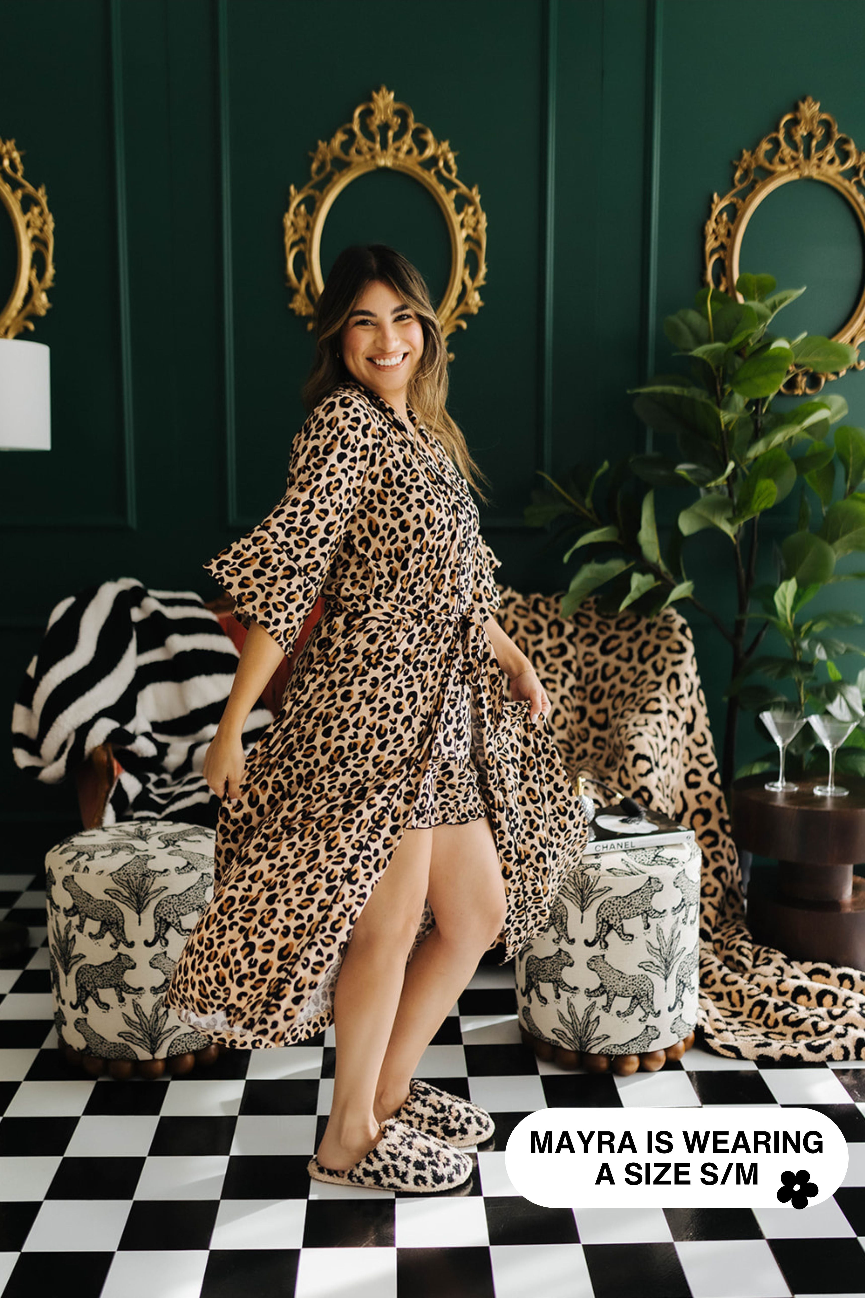 Woman wearing a leopard print robe in a stylish room with mirrors and plants.