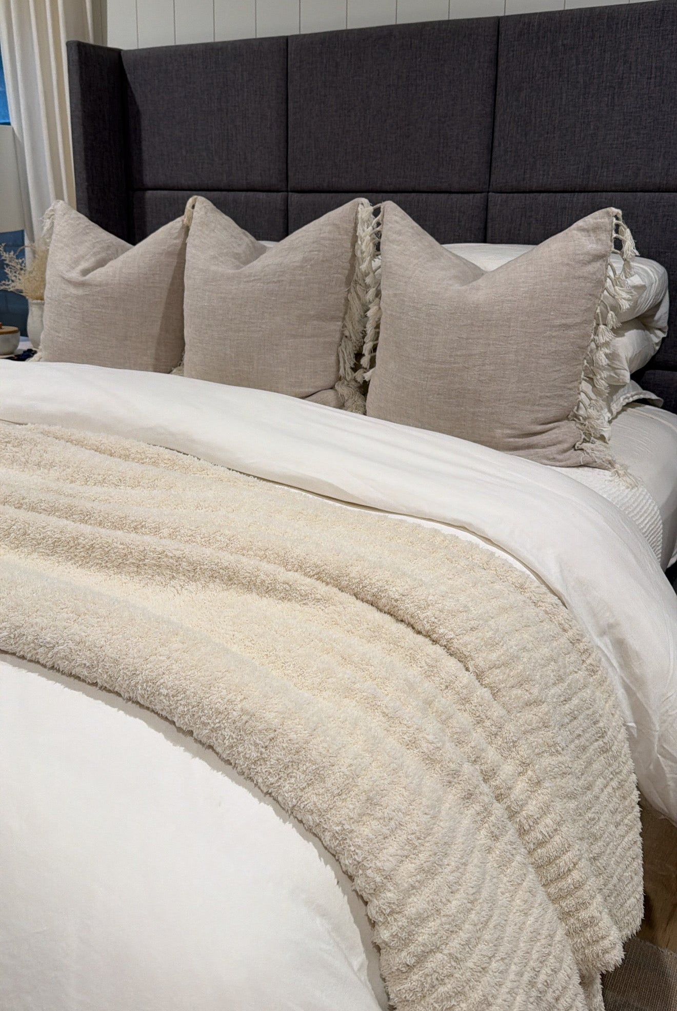 Neatly made bed with beige pillows and blanket against a dark headboard.