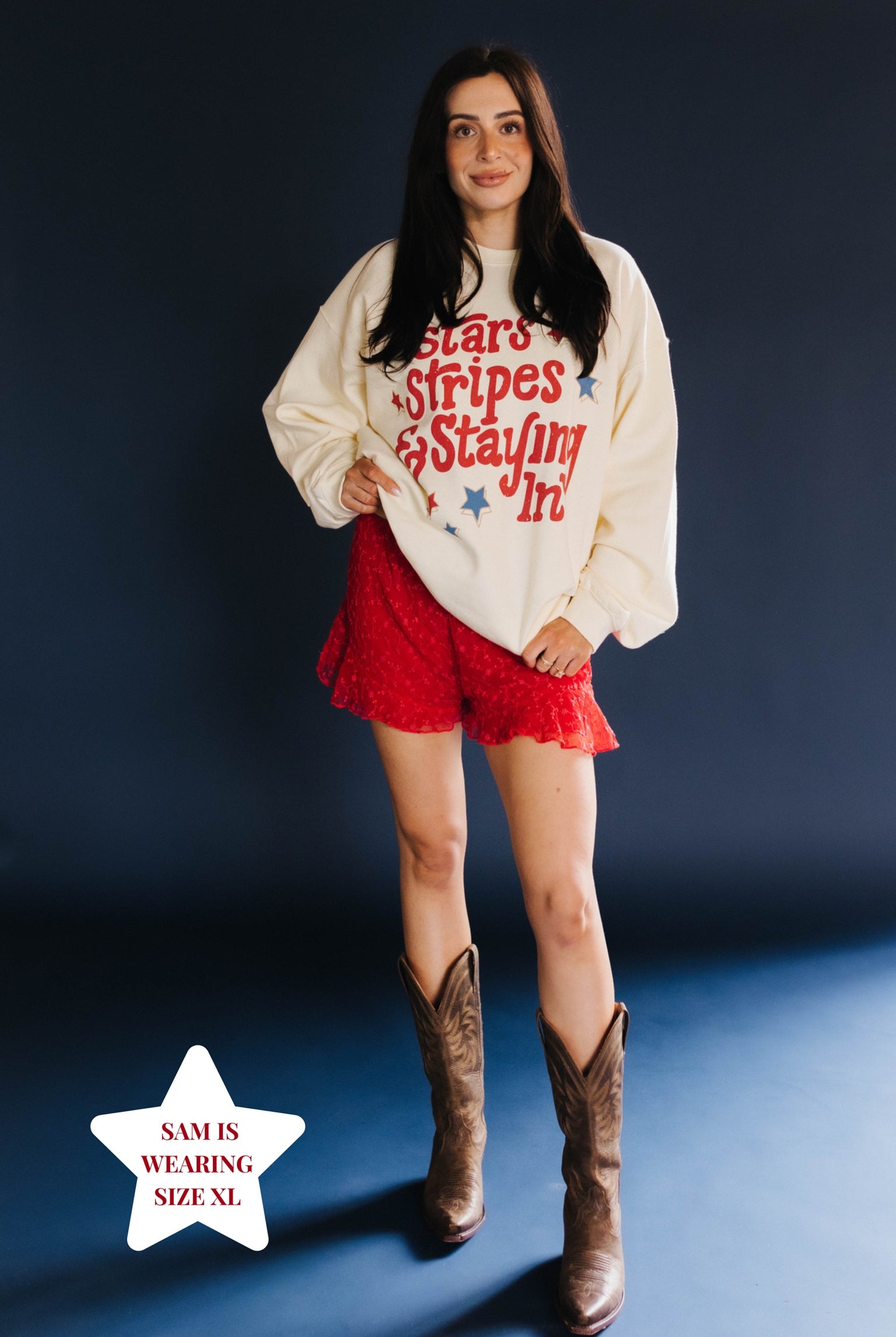 Woman wearing a graphic sweatshirt, red shorts, and brown boots on a dark background