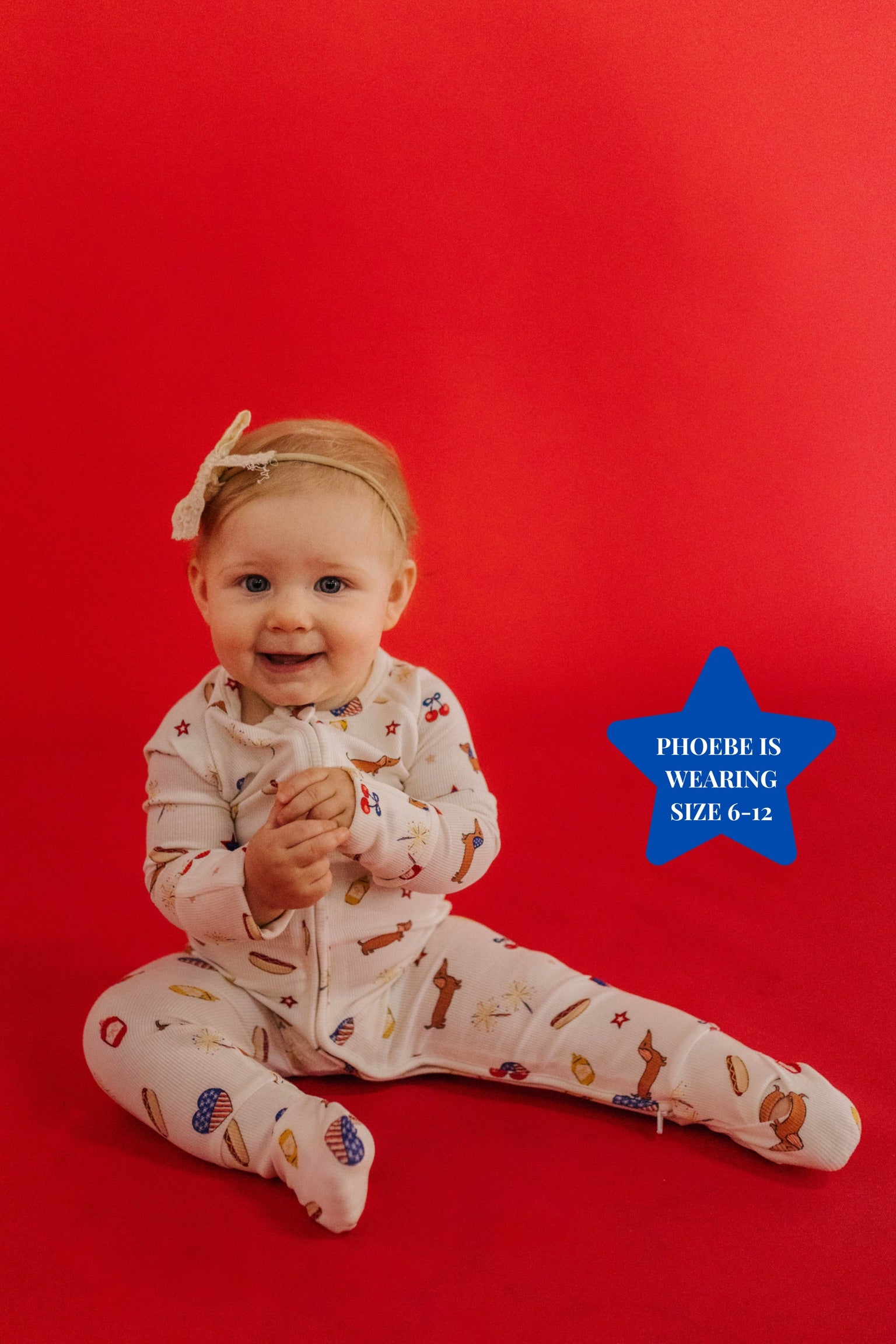 Baby sitting on a red background wearing pajamas with 4th of july icons