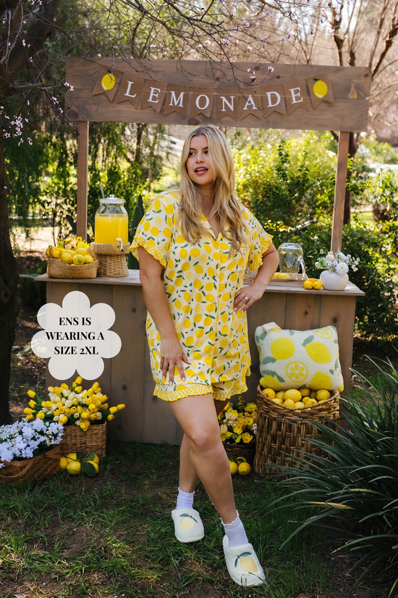 Woman in a yellow floral outfit standing next to a lemonade stand with lemon decorations. Size 2XL pjs