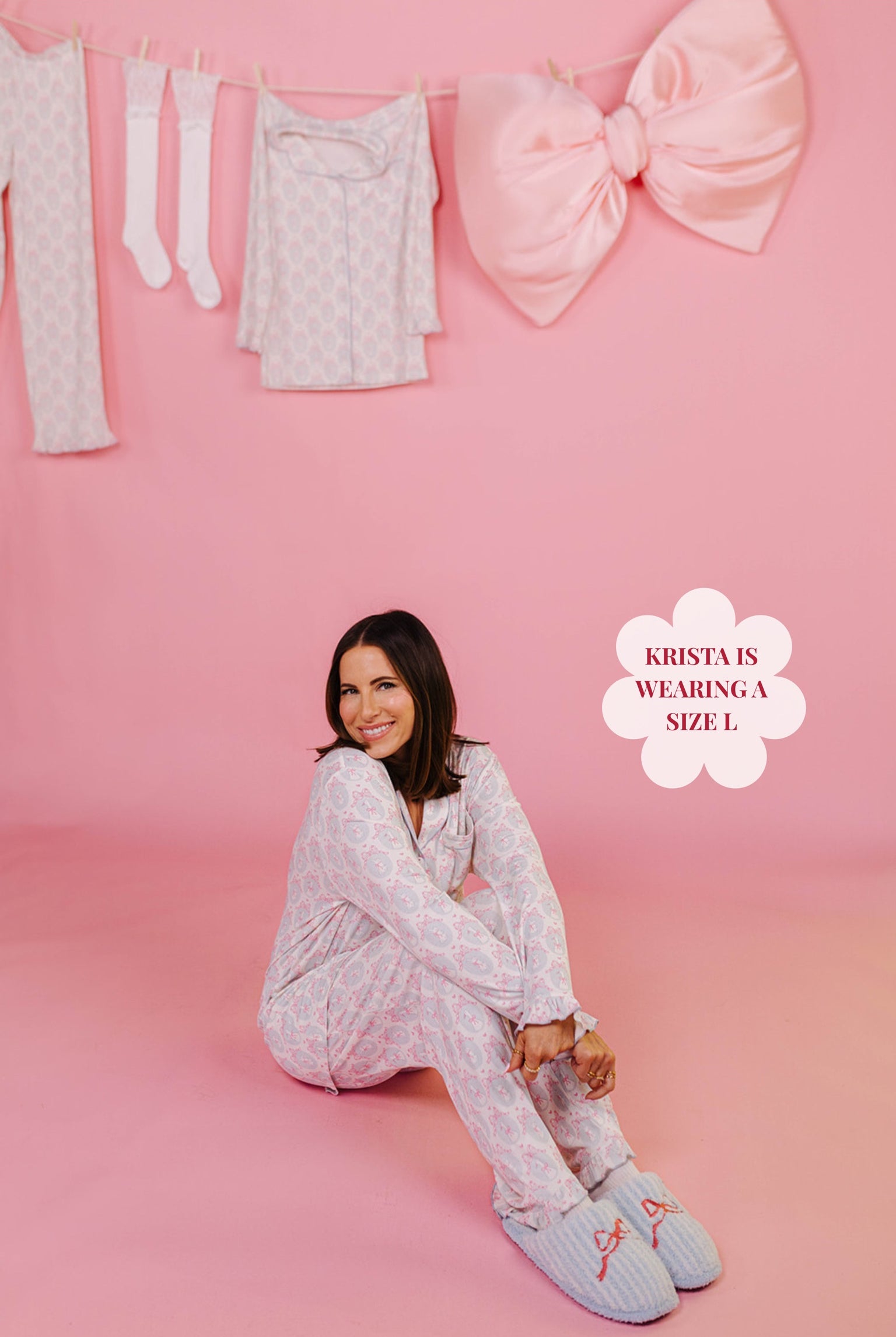 Woman sitting on a pink floor in her pajamas and a large pink bow in the background.