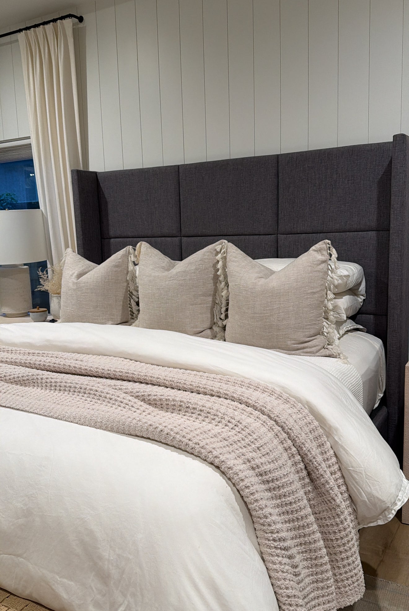 Bedroom with a bed featuring beige pillows and a textured blanket against a gray upholstered headboard.