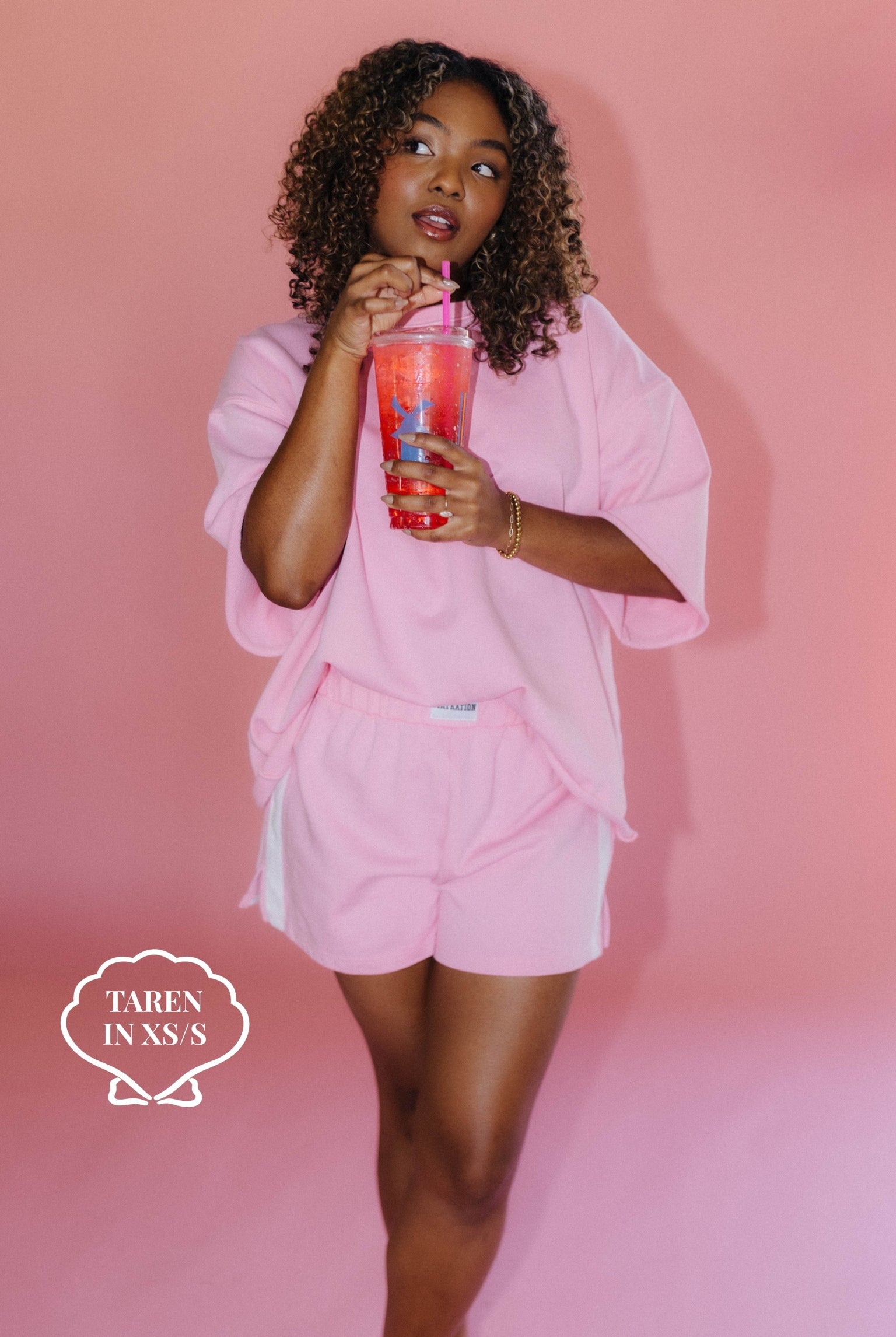 Woman in pink outfit holding a cup against a pink background