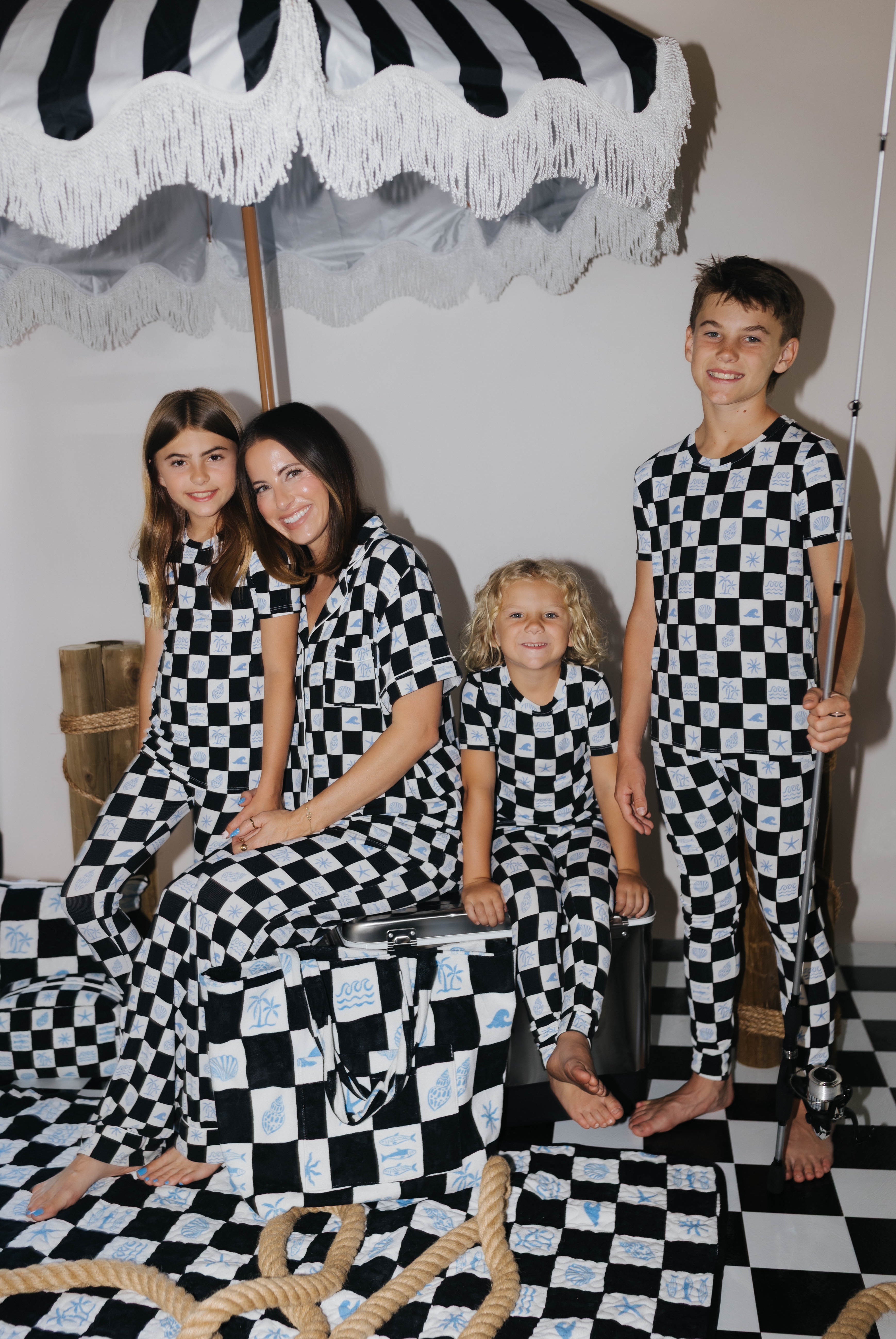 Family of four posing in black and white checkered outfits on a checkered floor with an umbrella in the background.