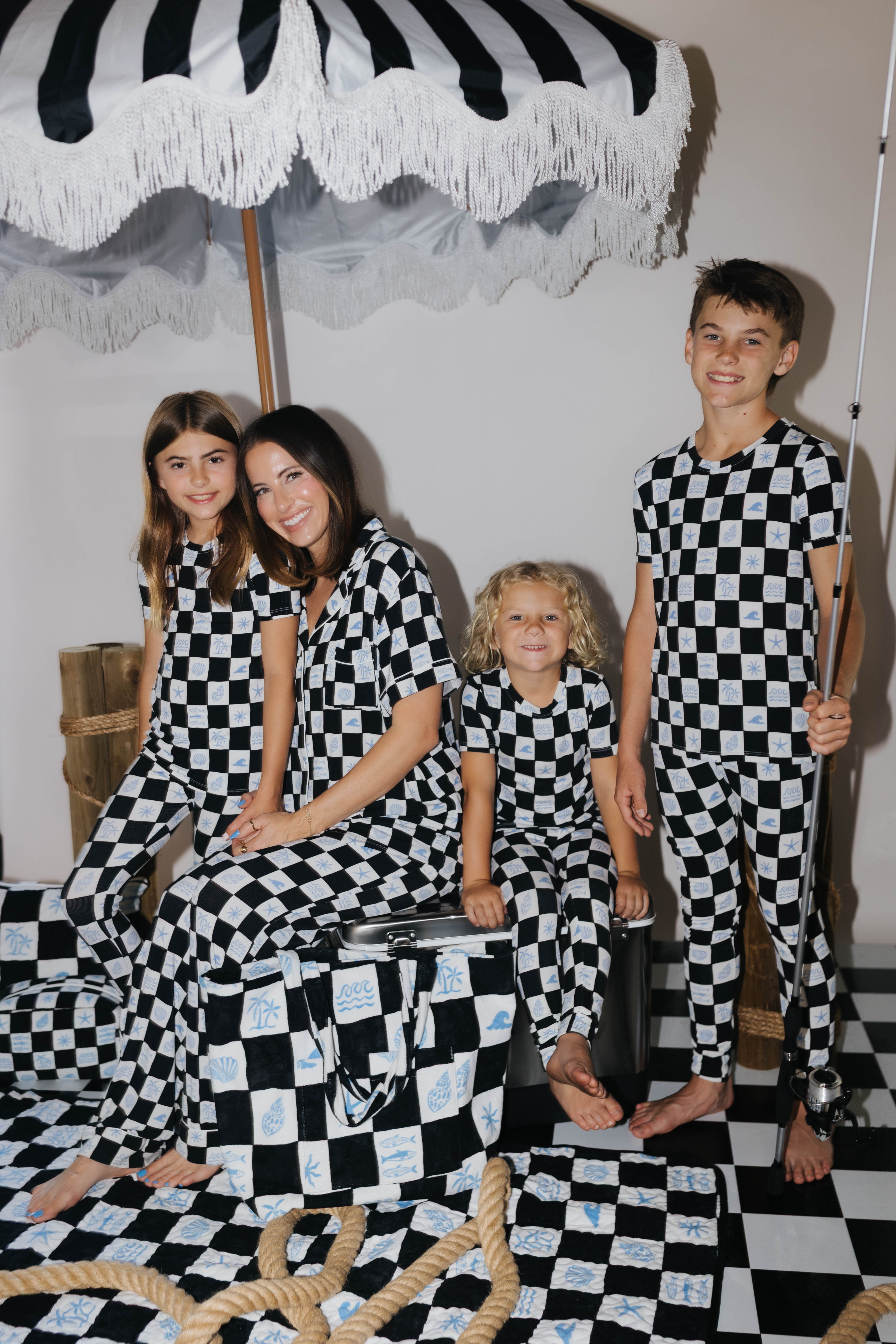 Family of four posing in black and white checkered outfits on a checkered floor with an umbrella in the background.