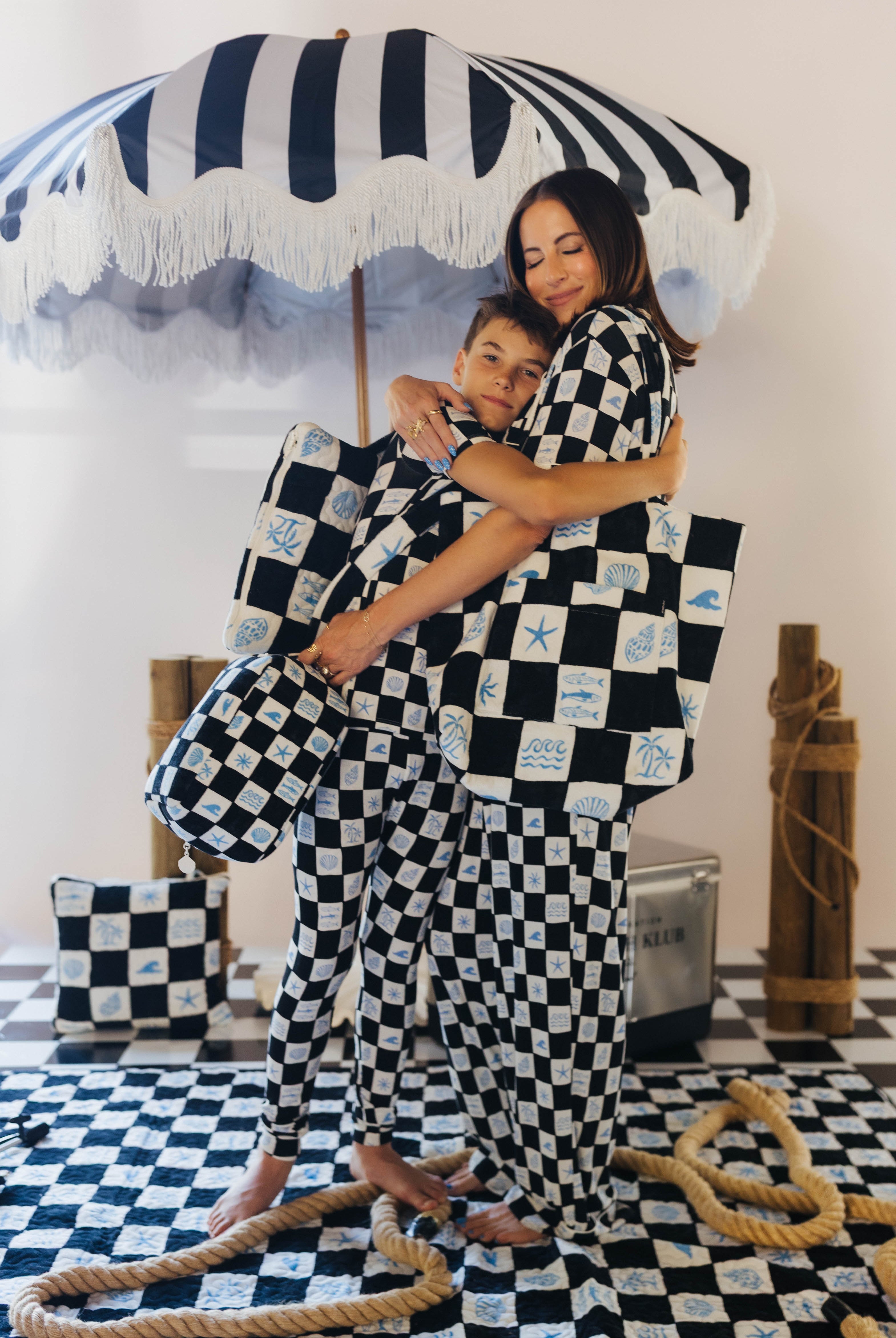 Woman and child hugging under a striped umbrella with checkered patterned fabric.
