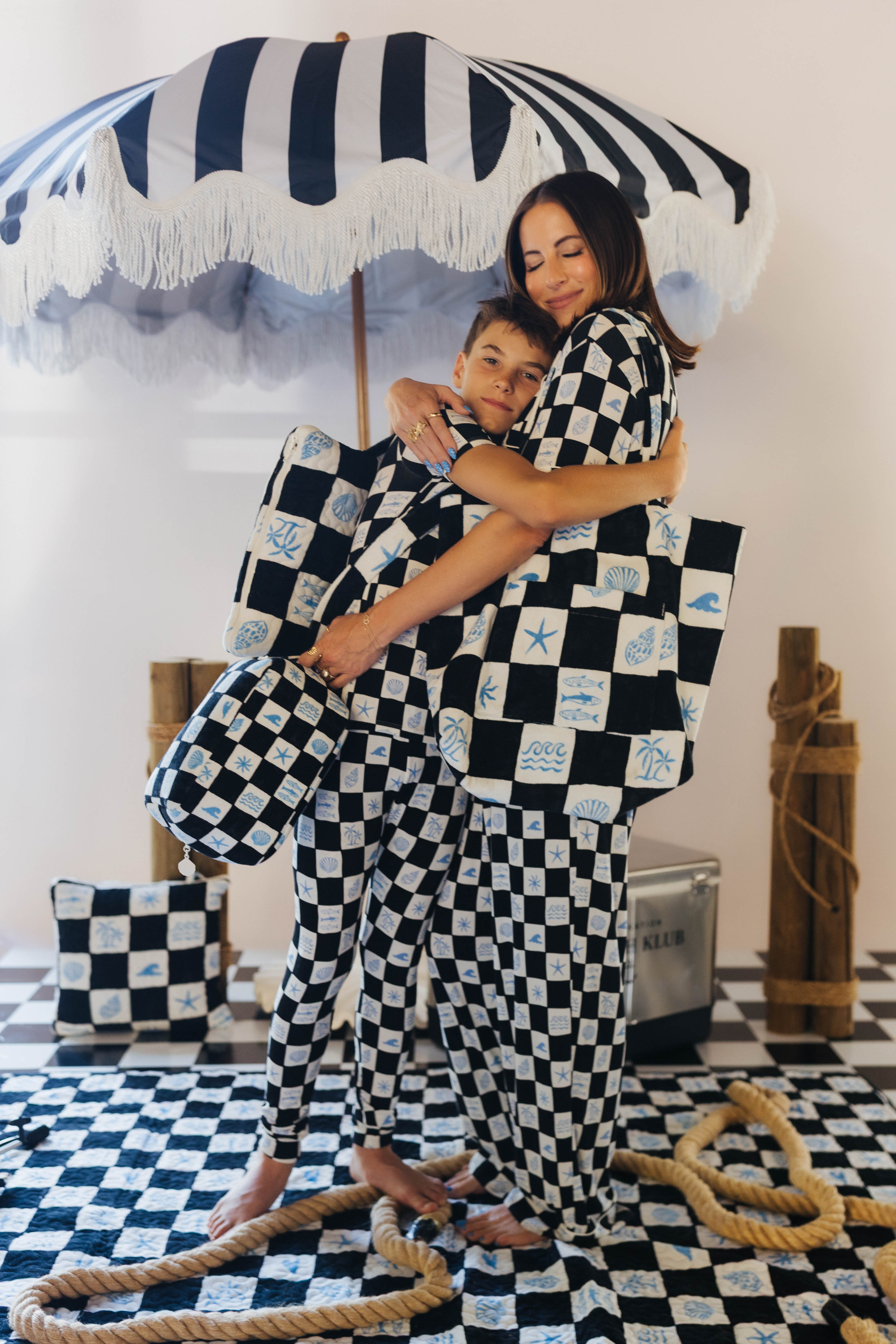 Woman and child hugging under a striped umbrella with checkered patterned fabric.