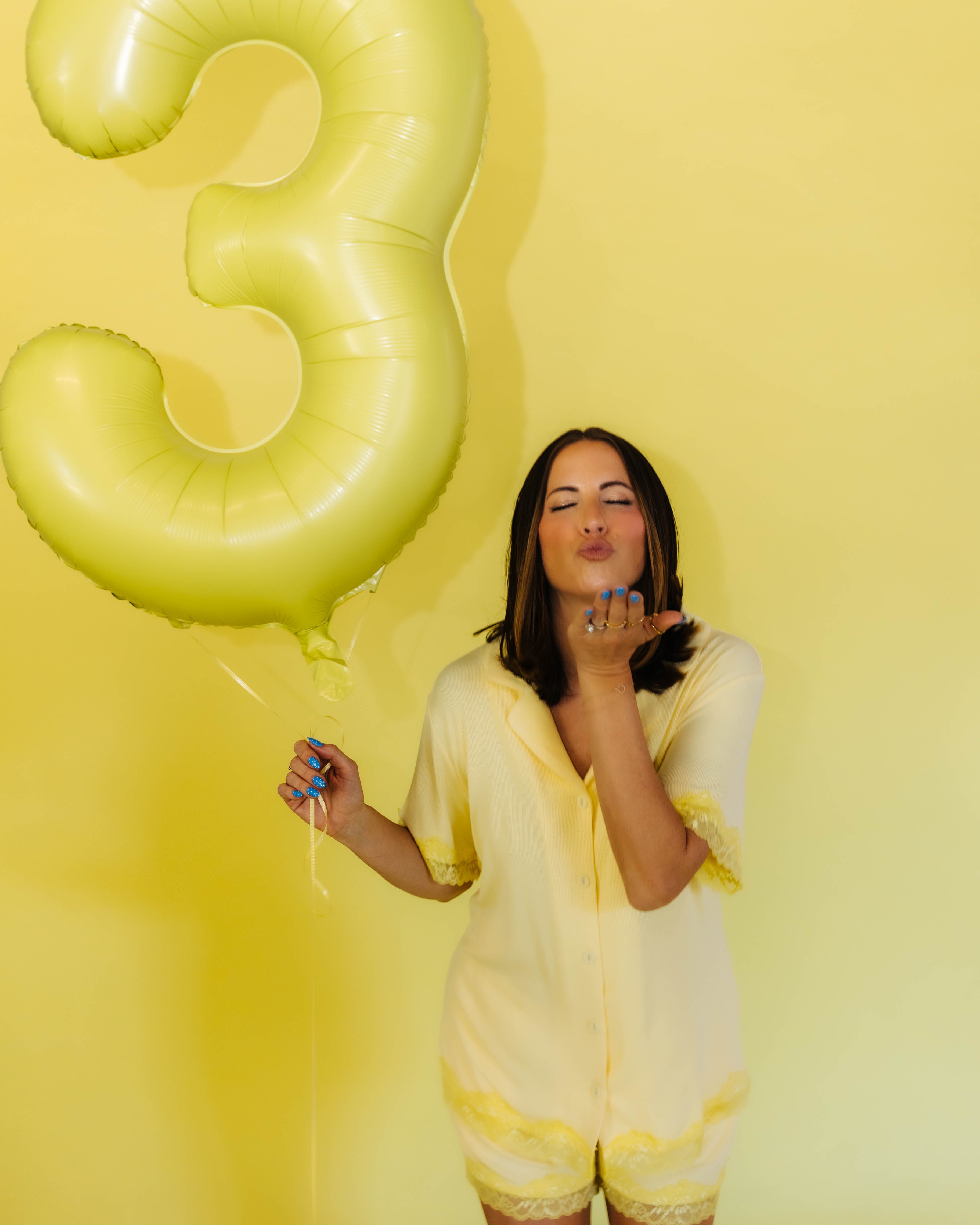 Krista in the yellow pjs blowing a kissy face holding a 3 balloon