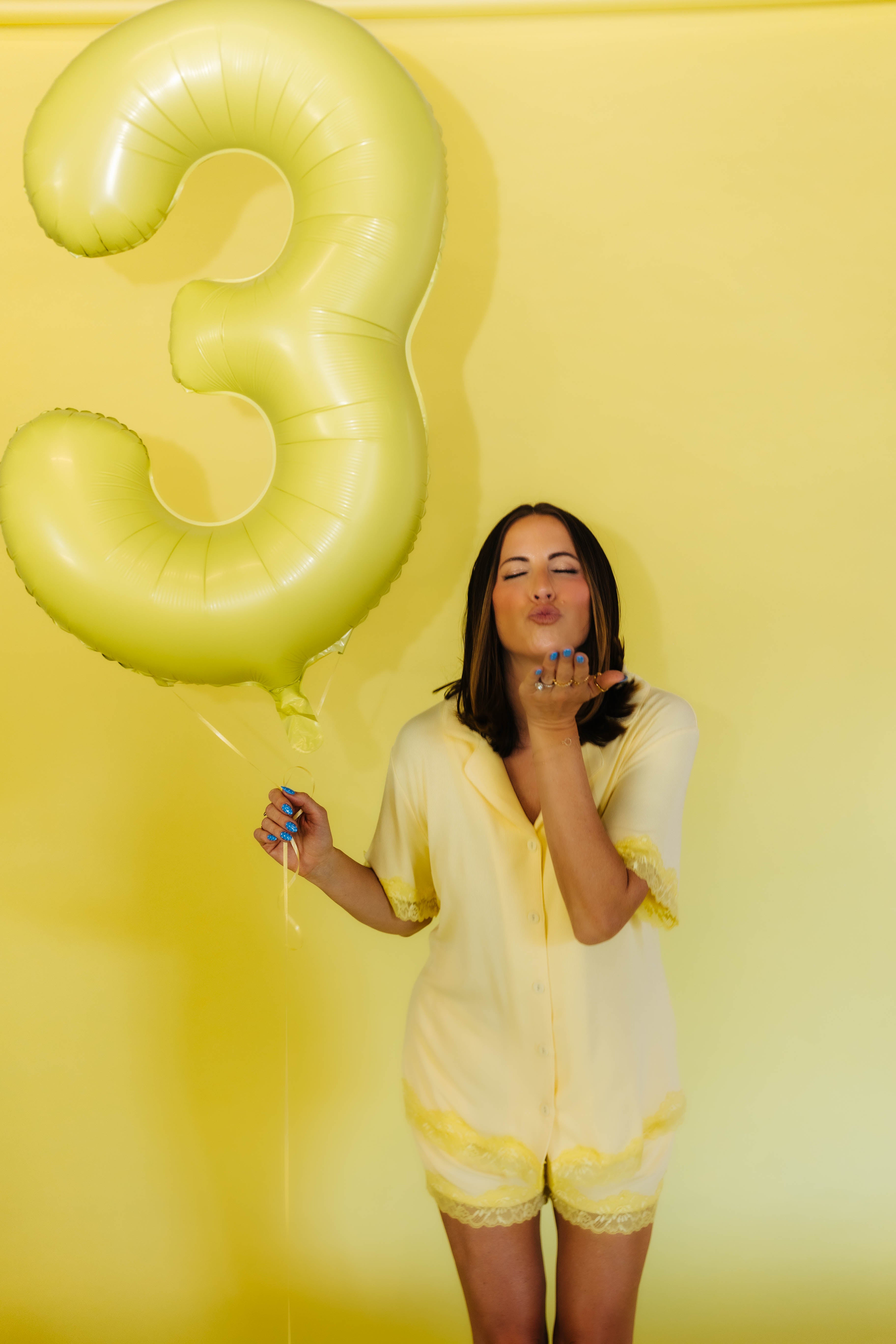 Krista in the yellow pjs blowing a kissy face holding a 3 balloon